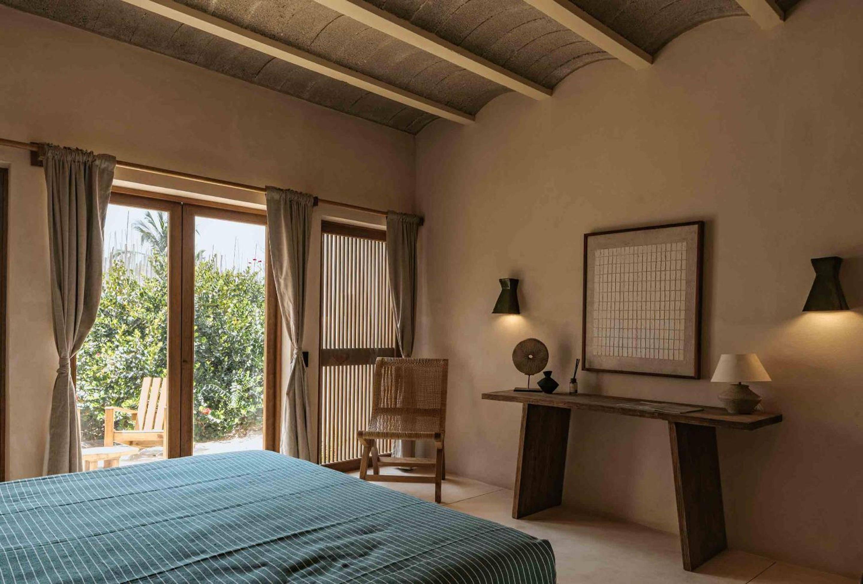 Natural light filters through woven bamboo screens in this serene bedroom, where exposed beam ceilings and handcrafted furnishings create an authentic Mexican coastal retreat.