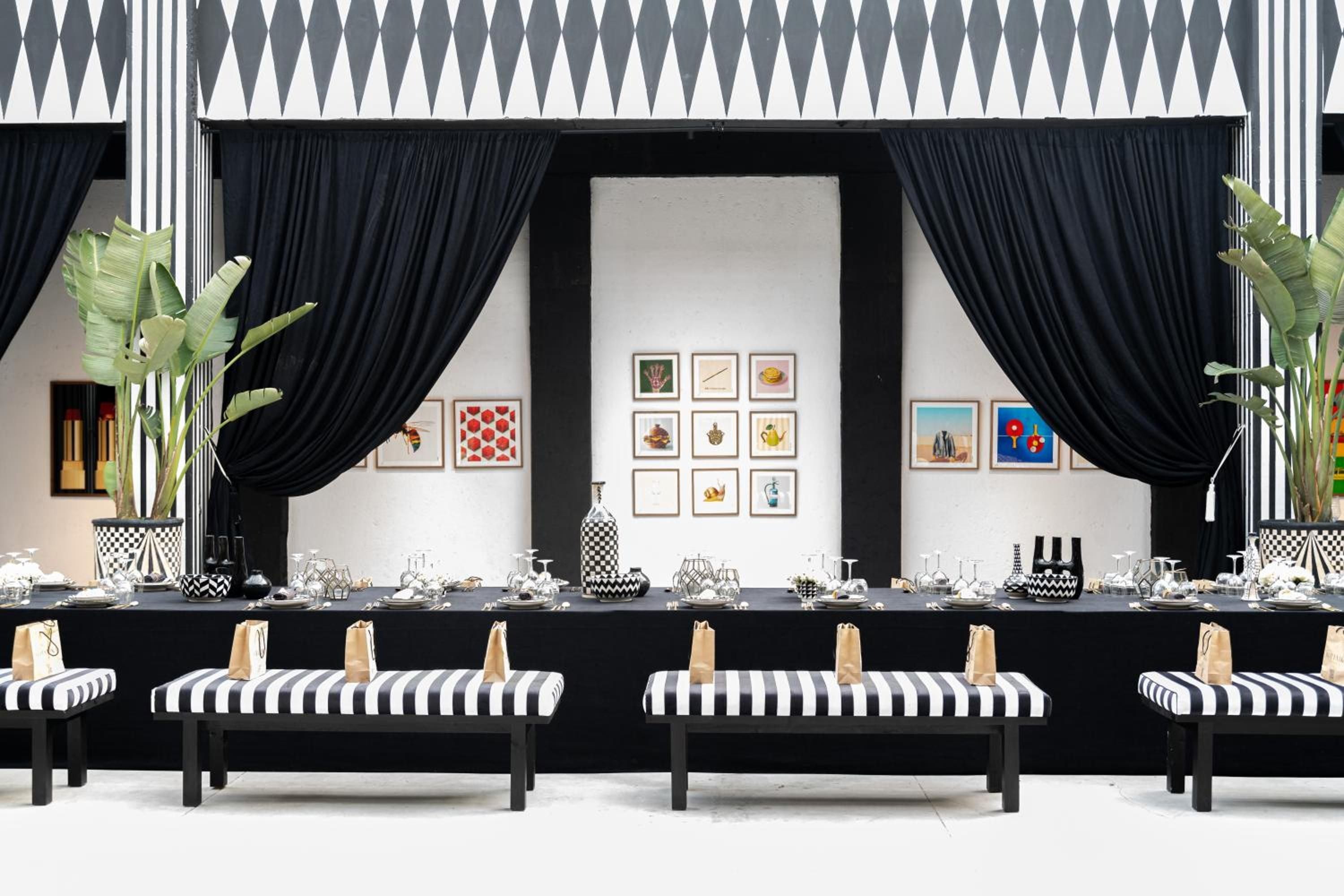 Bold black and white geometric patterns create theatrical drama in this dining pavilion, where Moroccan-inspired artwork and lush palms frame an elegantly set communal table.