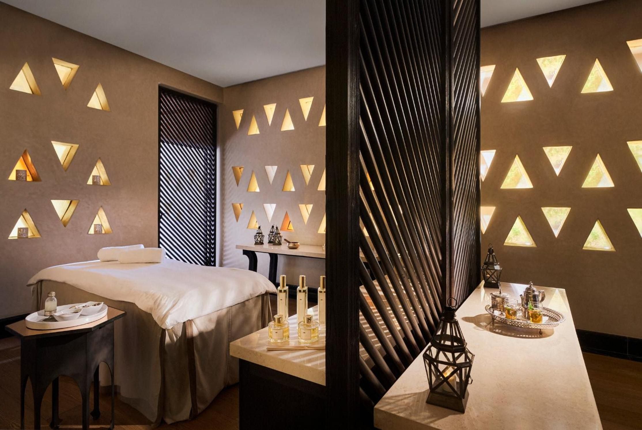 Triangular niches cast warm amber light across treatment walls while ornate lanterns and golden oils await in this serene sanctuary inspired by Moroccan craftsmanship.