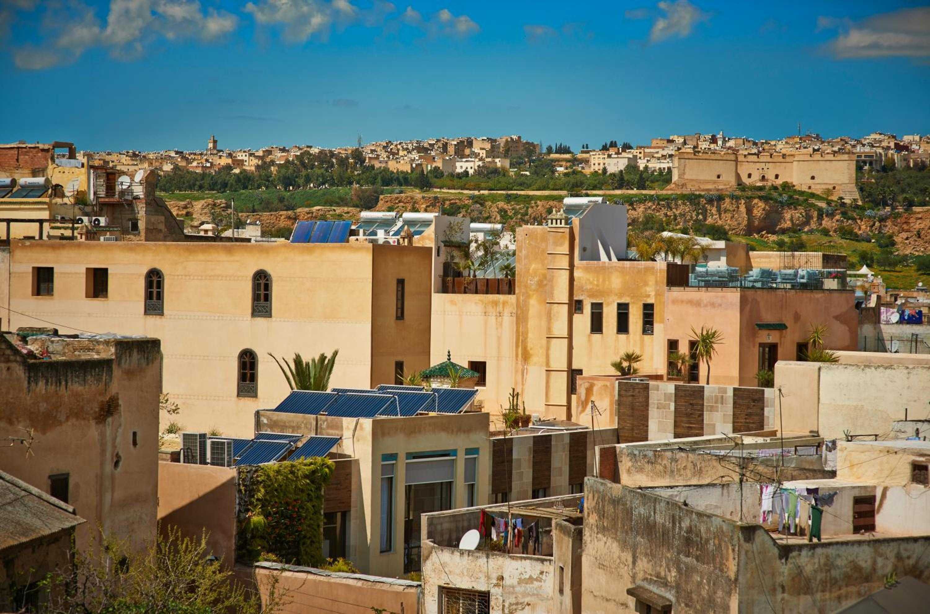 Ancient medina walls and traditional riads cascade across sun-baked terraces, where solar panels blend seamlessly with centuries-old Moroccan architecture under brilliant blue skies.
