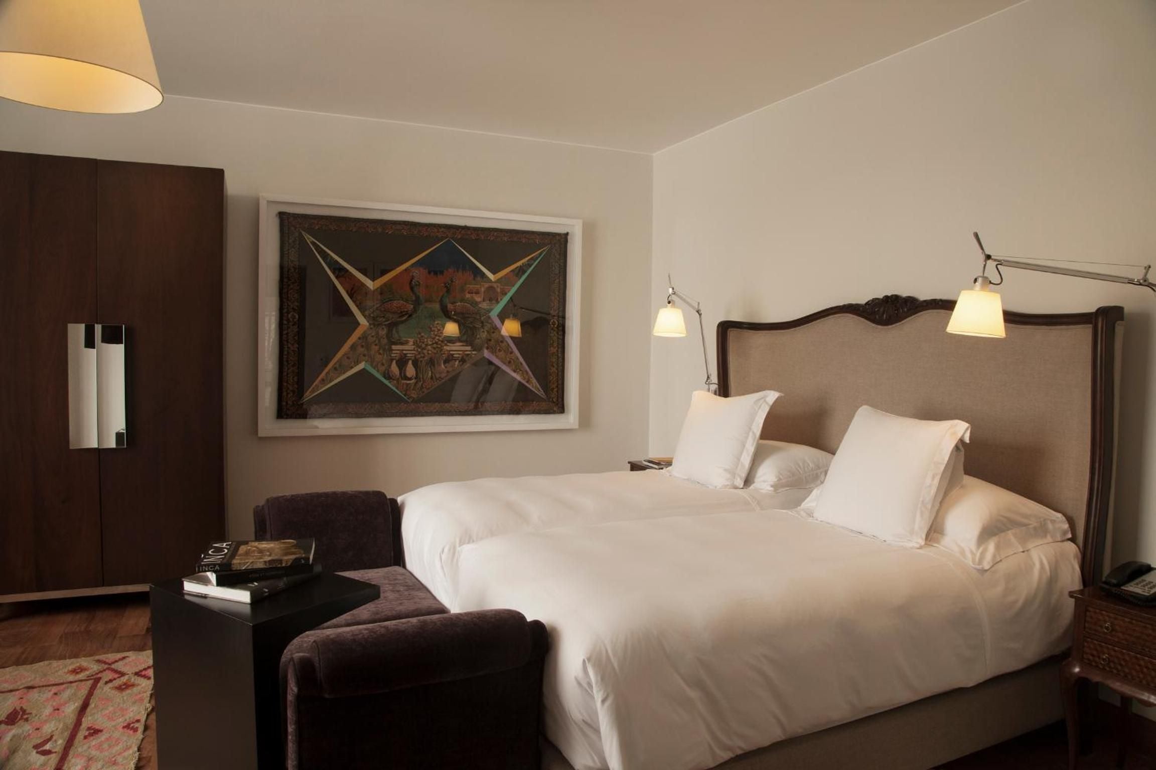 Warm bedside sconces cast a golden glow over crisp white linens and rich wood furnishings, while contemporary art adds unexpected color to this intimate sanctuary.