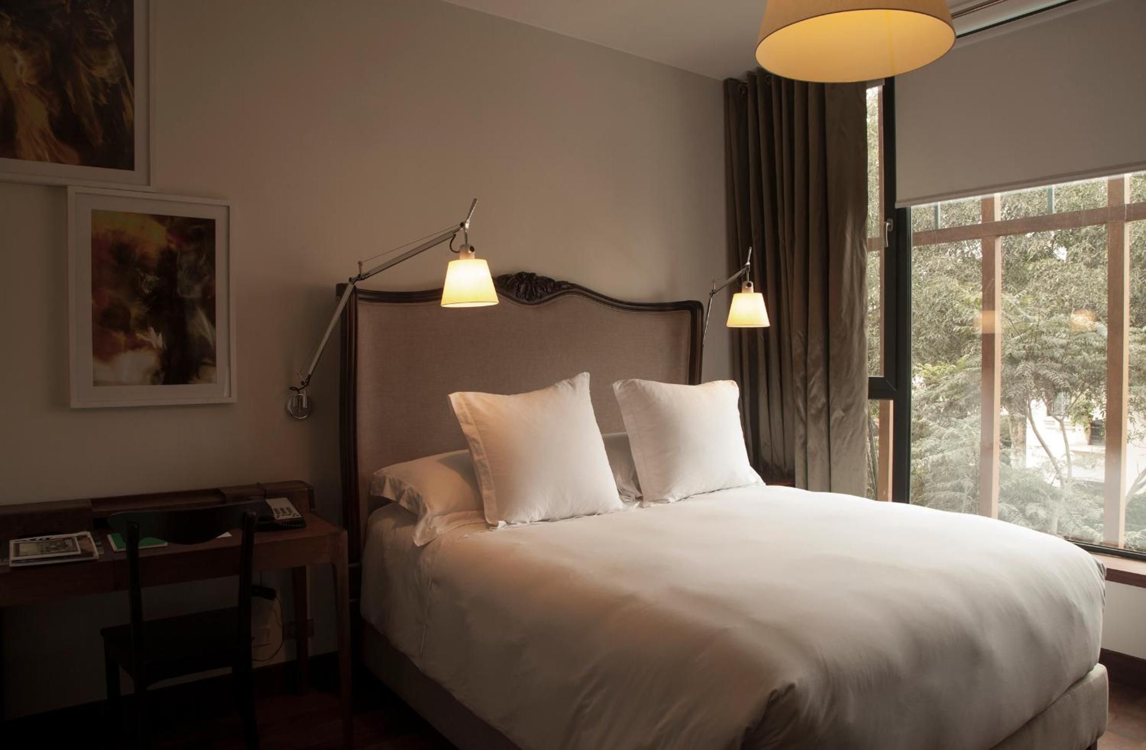 Warm pendant lamps cast intimate pools of light over crisp white linens, while floor-to-ceiling windows frame verdant garden views in this thoughtfully appointed guest room.