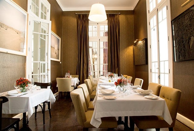 Warm amber walls and crisp white linens create an intimate dining atmosphere, where French doors flood the sophisticated space with golden afternoon light.