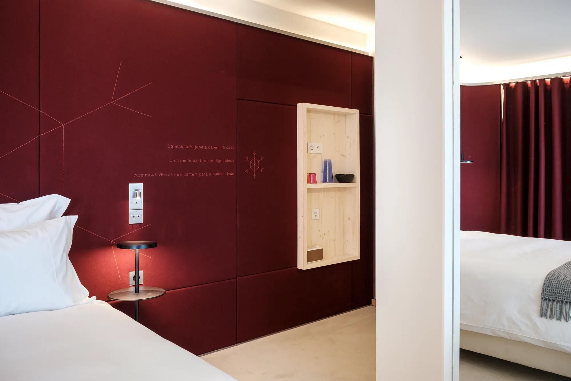 Burgundy panels etched with Portuguese poetry frame a recessed niche, where artisanal ceramics catch soft light in this thoughtfully curated guest room.