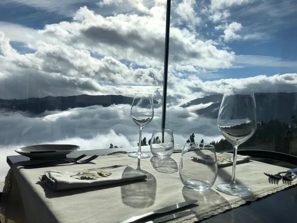 Wine glasses catch mountain reflections at this cloud-kissed terrace, where dramatic peaks emerge through morning mist beyond the elegantly set table.