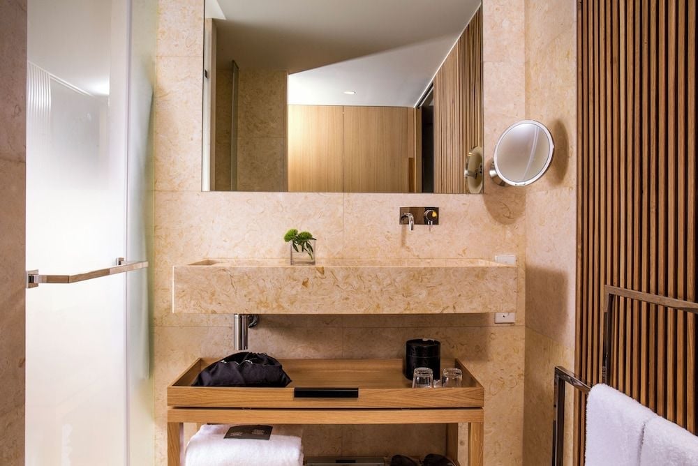 Warm travertine and sleek wood slats create a spa-like sanctuary where modern minimalism meets tactile luxury in this thoughtfully appointed guest bathroom.