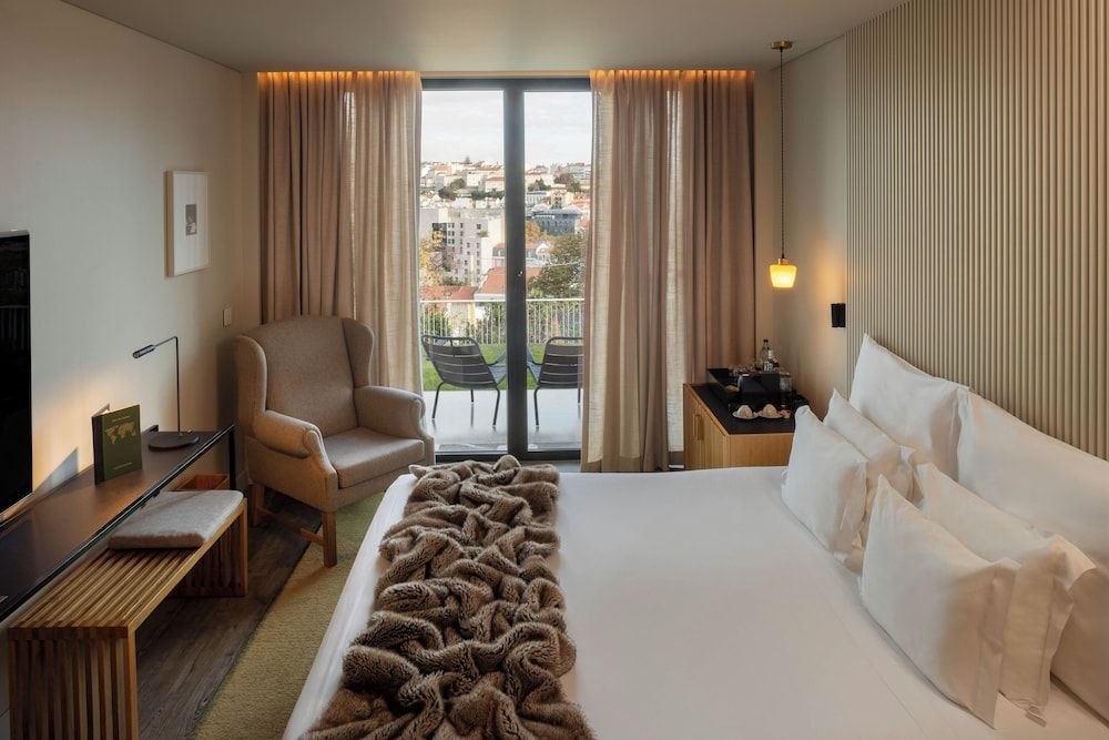 Warm amber lighting and textured wood panels create intimate sanctuary vibes, while floor-to-ceiling windows frame Lisbon's terracotta rooftops and rolling hills beyond the private terrace.