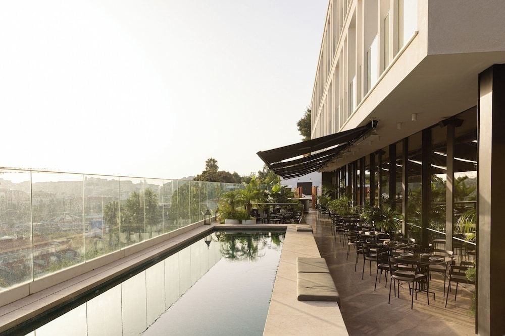 Sunlight dances across the rooftop pool's mirror-like surface while diners settle into the shaded terrace, Lisboa's rolling hills stretching beyond glass railings.