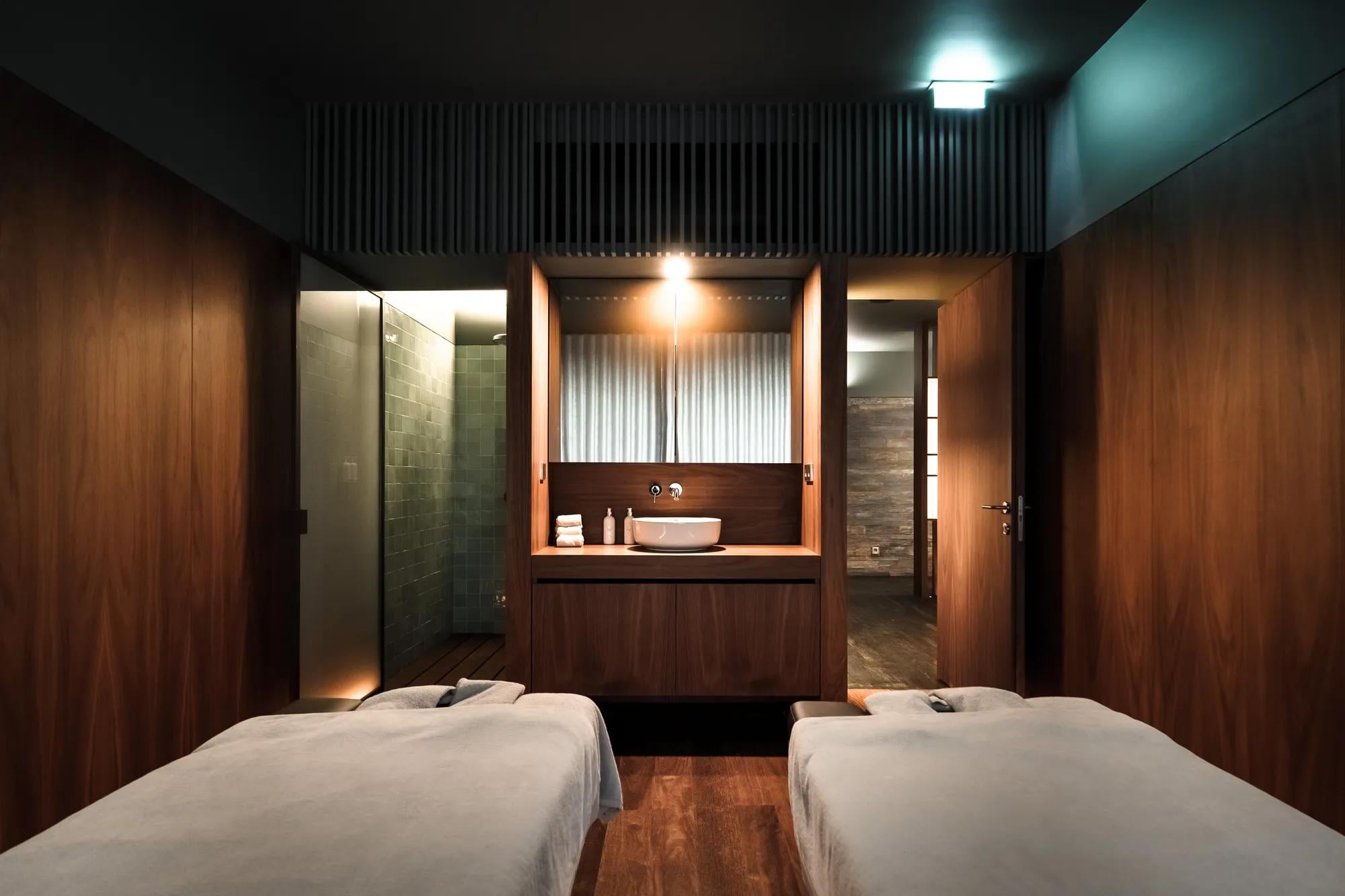 Warm wood paneling and soft lighting create an intimate sanctuary in the couples treatment room, where polished stone and clean lines invite deep relaxation.