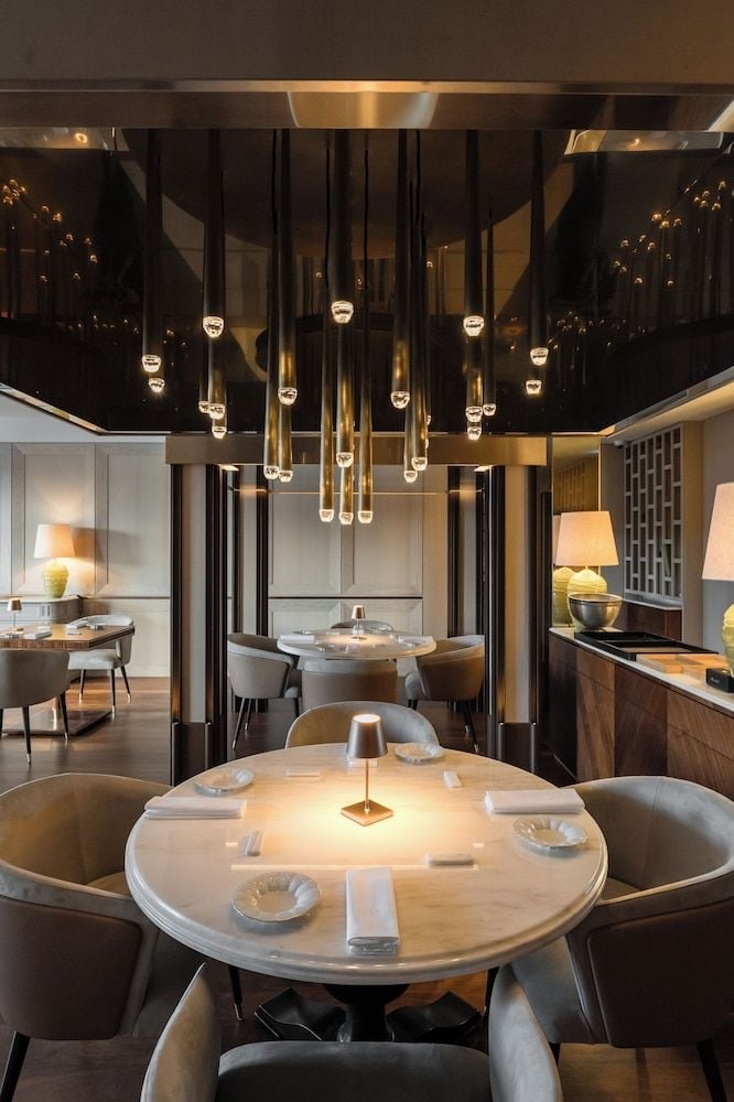 Pendant lights cascade like golden droplets above intimate round tables, where brass accents and plush seating create an atmosphere of understated Portuguese elegance.