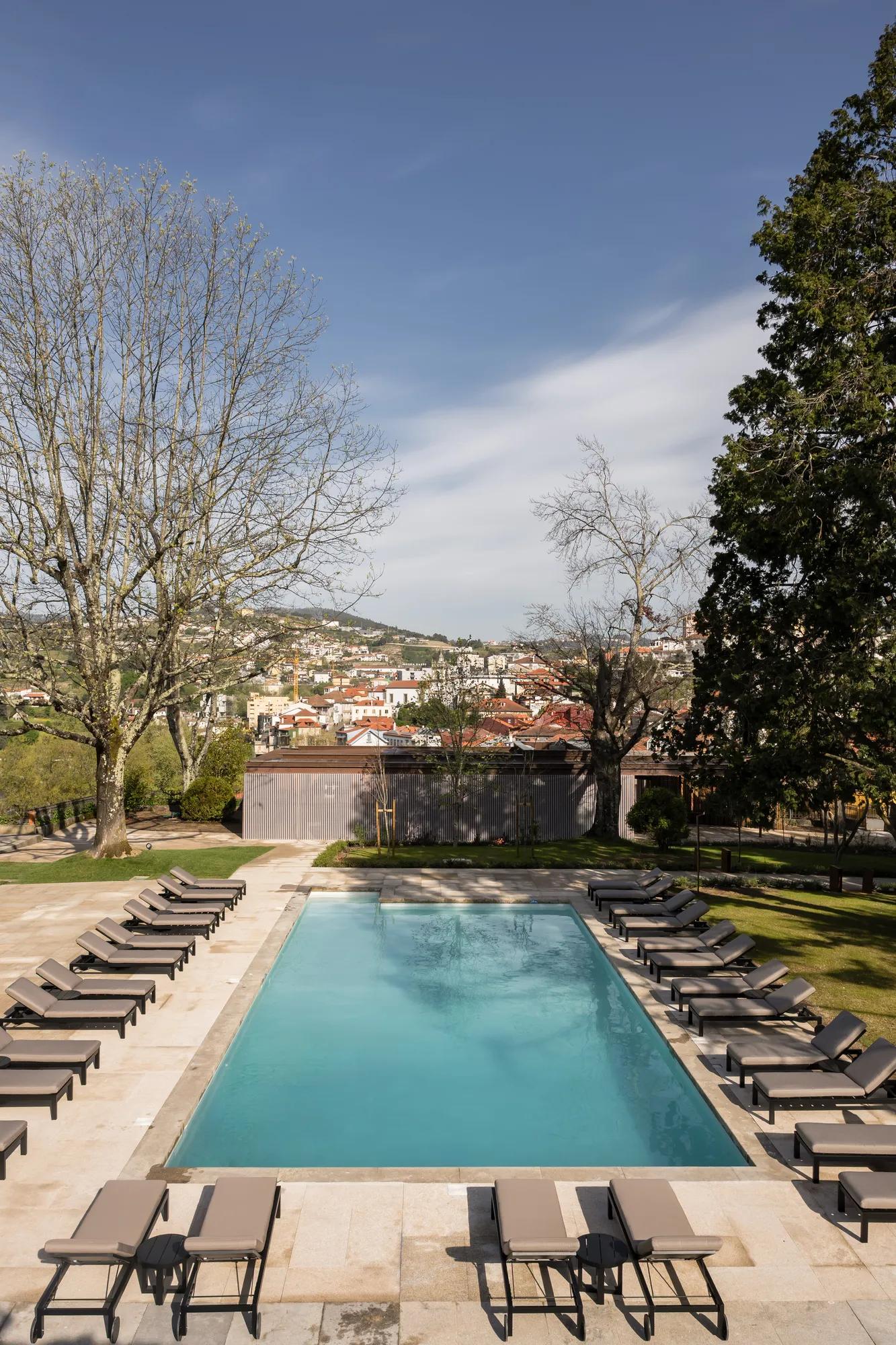 Lounge chairs frame the infinity pool's crystalline waters, while red-tiled rooftops of historic Amarante cascade down verdant hillsides beyond weathered stone walls.