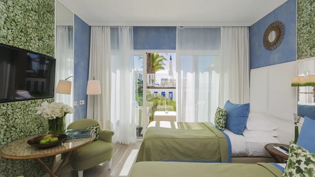 Crisp white linens meet Mediterranean blues in this elegantly appointed room, where botanical wallpaper and sheer curtains frame glimpses of Algarve coastline beyond.