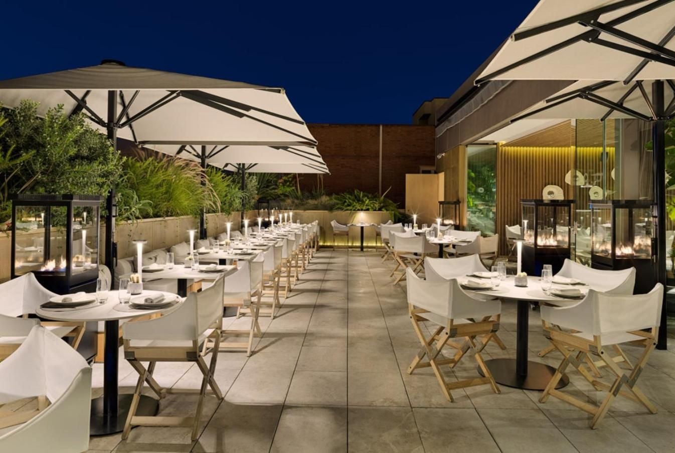 Barcelona's skyline provides a dramatic backdrop for alfresco dining, where crisp white linens and warm candlelight create an intimate terrace atmosphere under starlit skies.