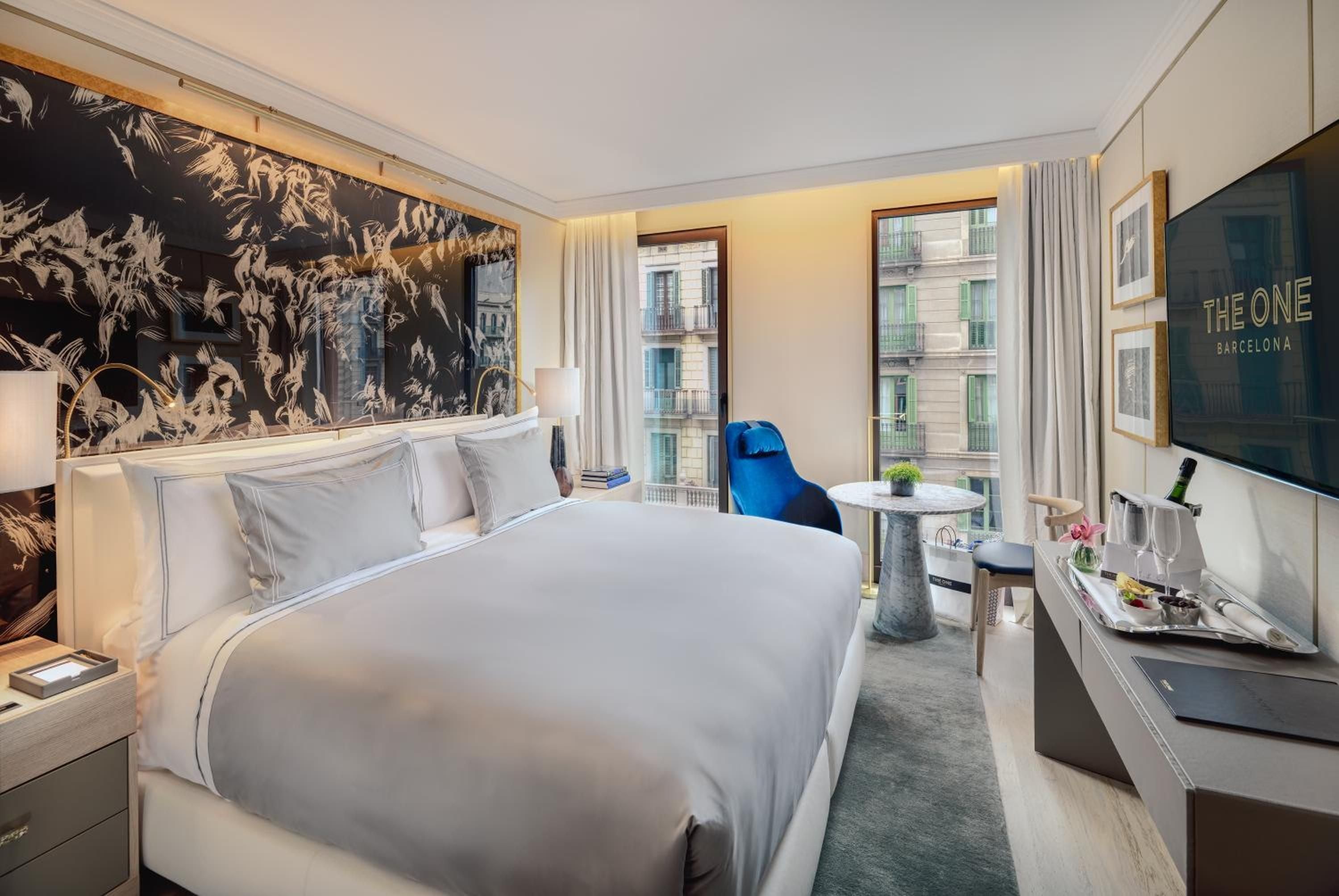 Botanical wallpaper creates an intimate backdrop in this Barcelona suite, where warm lighting meets crisp linens and windows frame the city's historic architecture beyond.