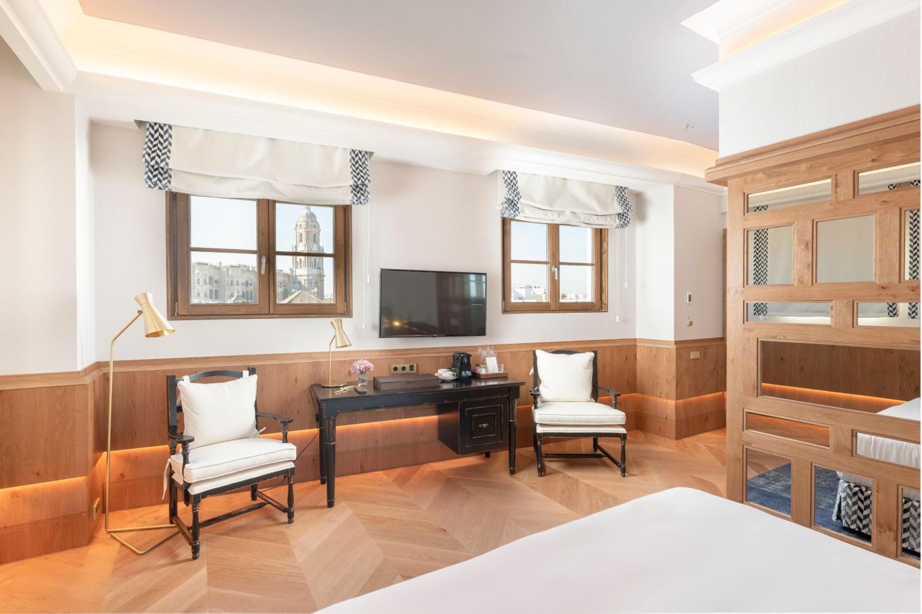Warm wood paneling and chevron-patterned textiles create an intimate retreat where golden task lighting illuminates handcrafted details and historic city views unfold beyond casement windows.