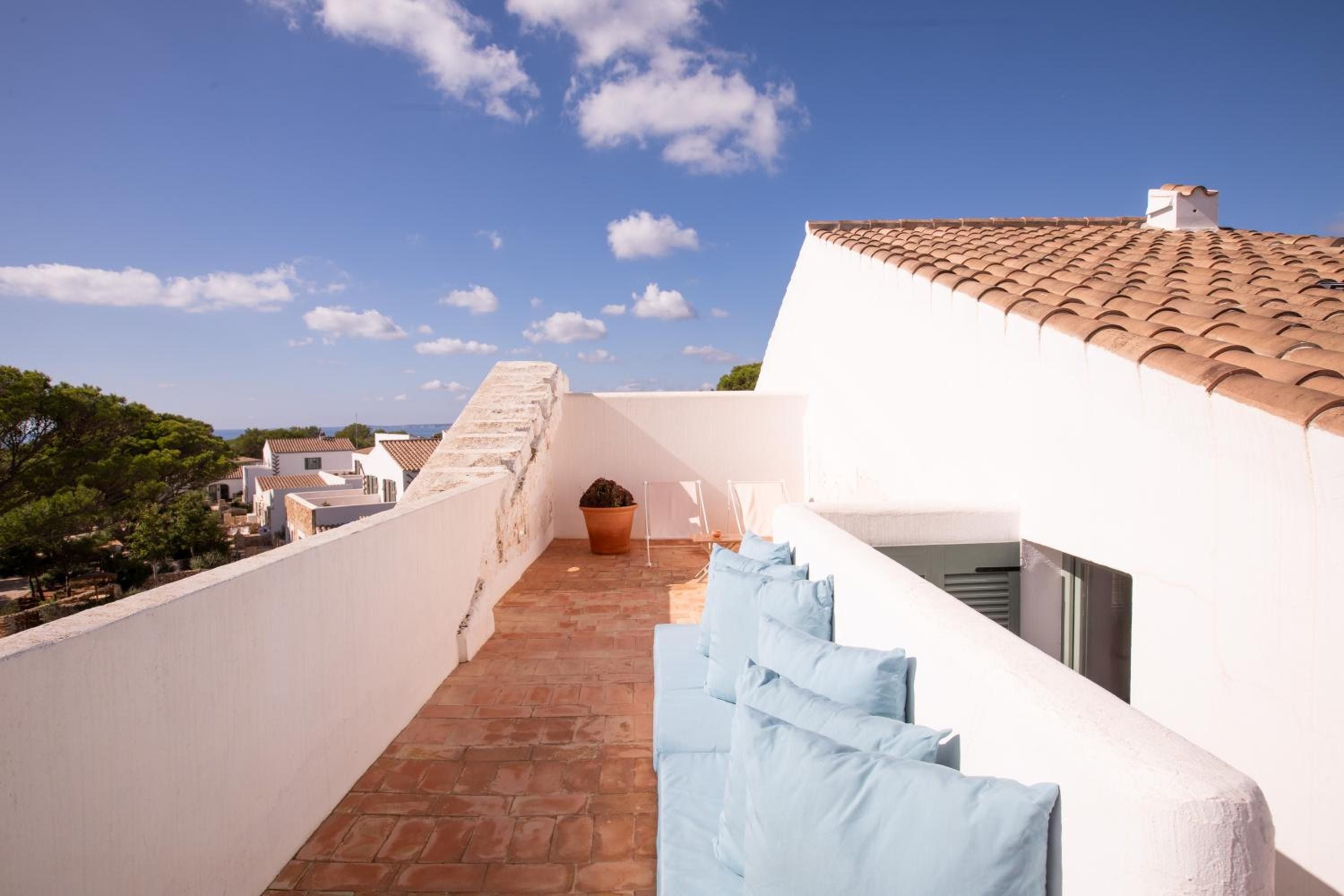 Terracotta tiles warm underfoot as Mediterranean breezes drift across this whitewashed rooftop terrace, where powder-blue cushions invite lazy afternoons beneath endless Balearic skies.