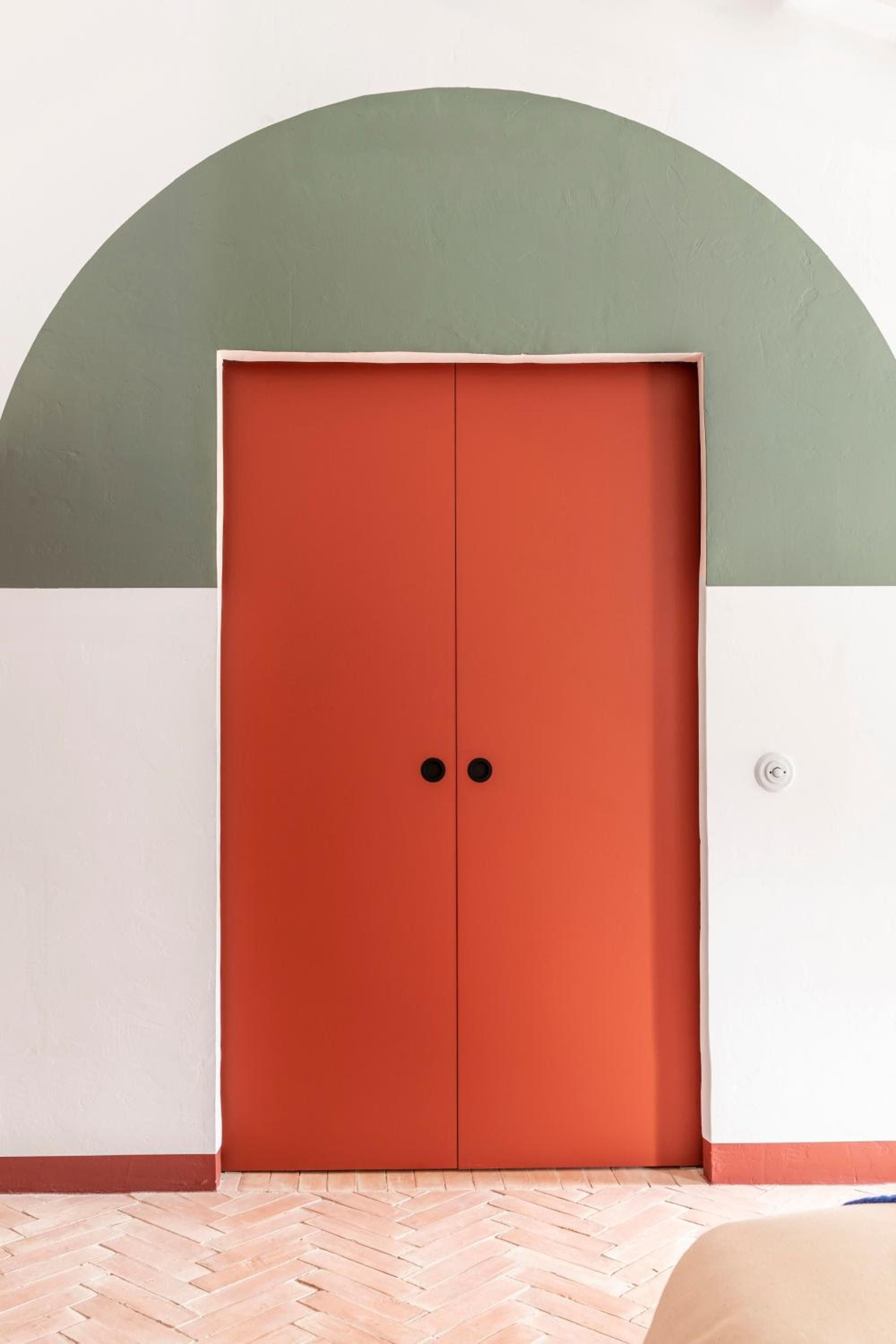 Bold tangerine doors punctuate sage-green archways, creating striking geometric moments that define Cap Menorca's playful yet sophisticated Mediterranean design language.