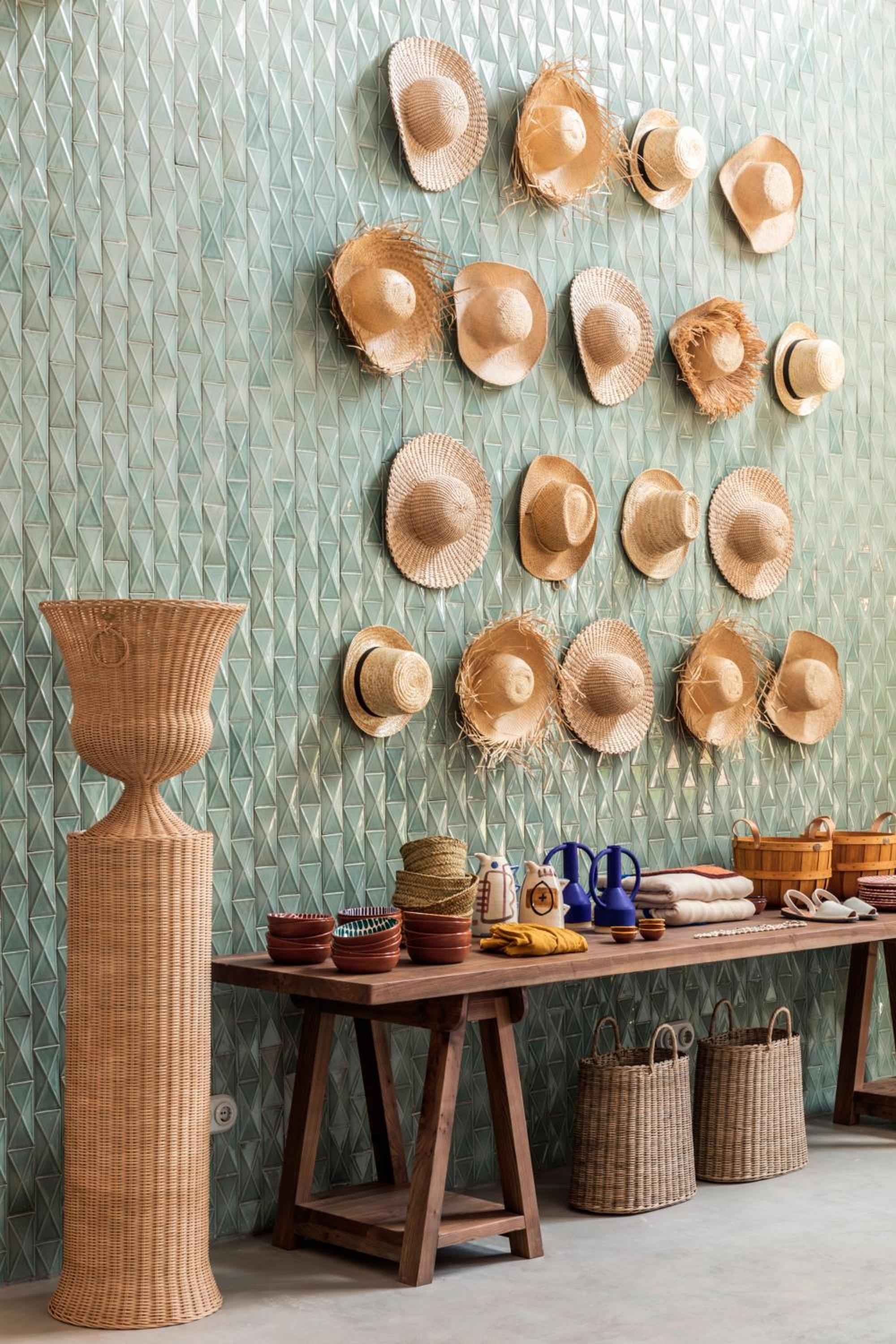 Natural woven hats create an artful display against geometric wallpaper, while handcrafted baskets and ceramics showcase the island's rich artisanal heritage in every corner.