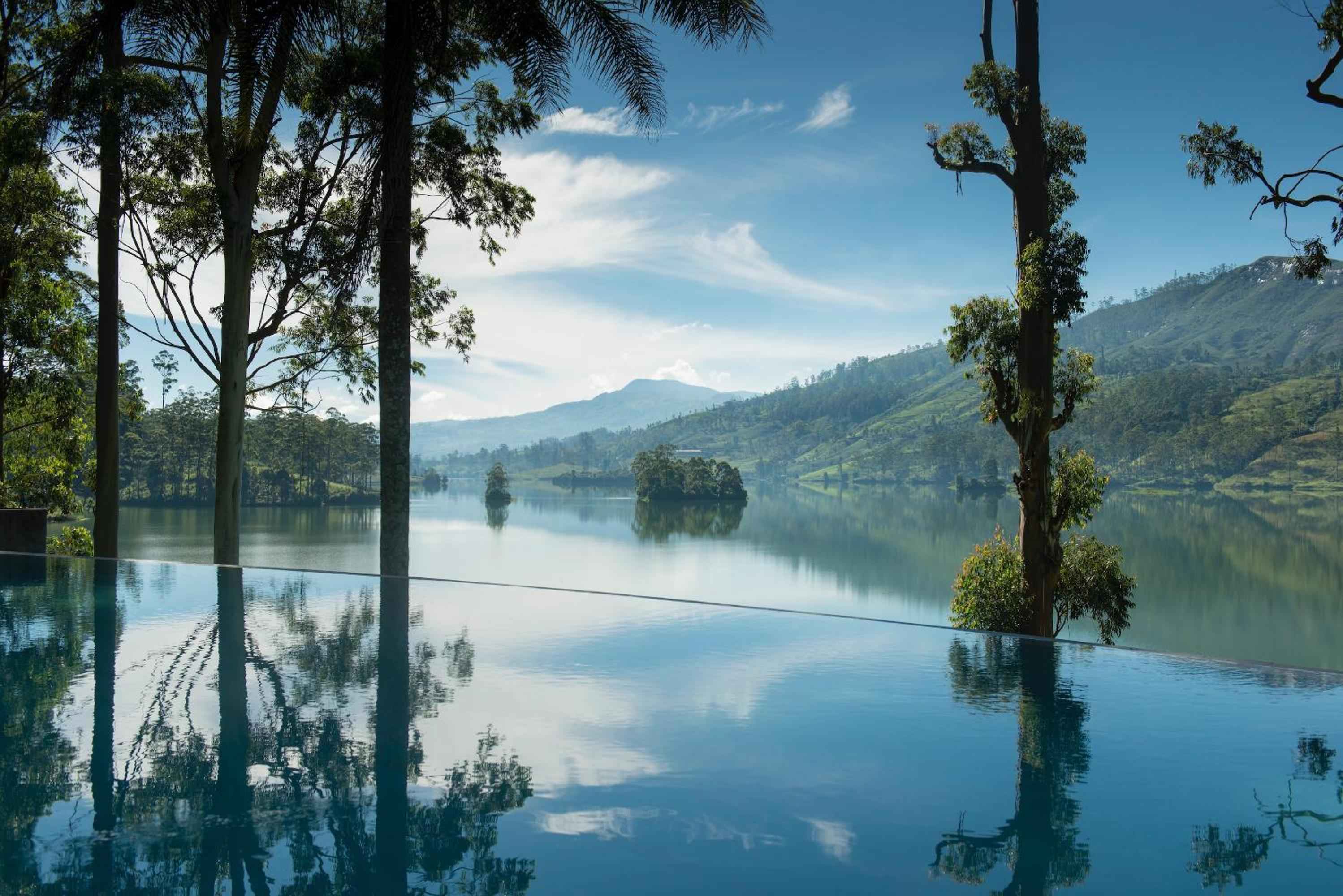 Morning mist rises from the lake as Ceylon Tea Trails' infinity pool mirrors rolling emerald hills, creating a seamless canvas of water and wilderness in Sri Lanka's highlands.