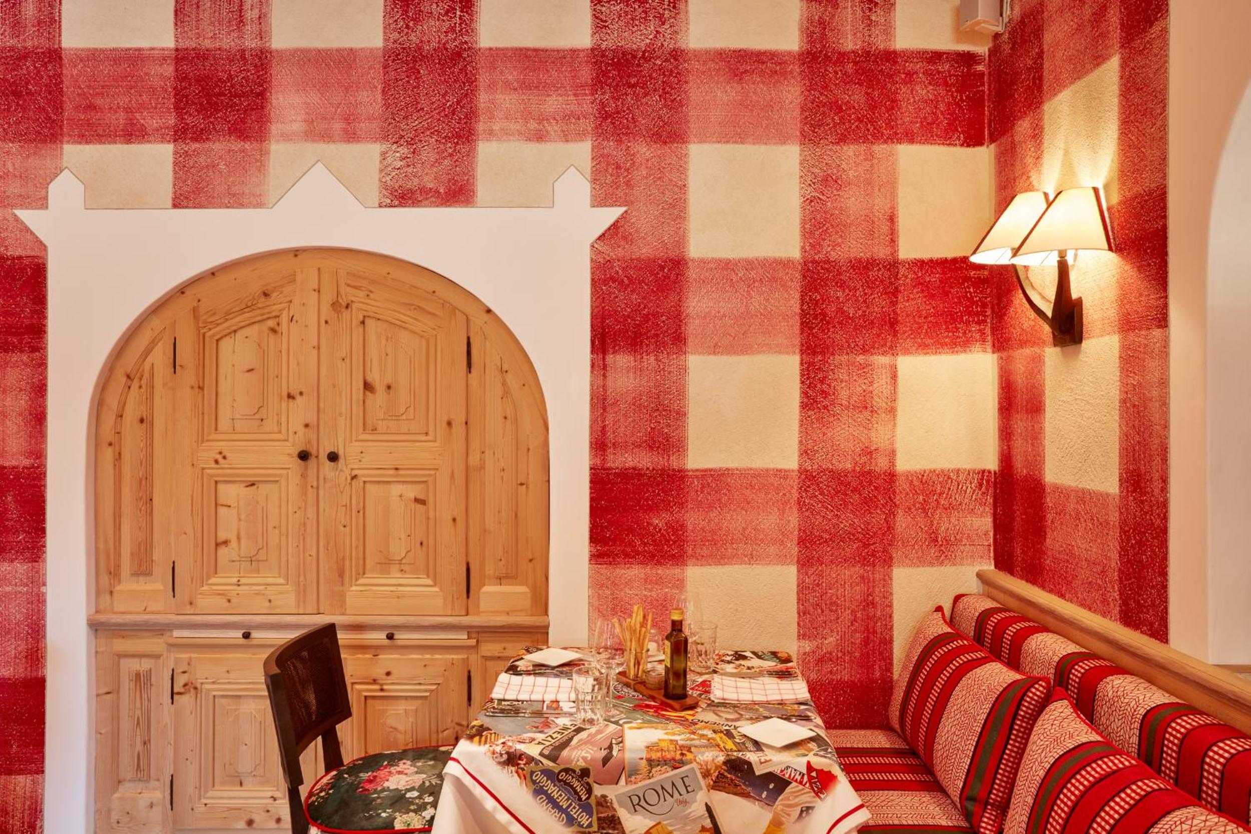 Red gingham wallpaper and Alpine woodwork create an intimate dining nook where traditional Tyrolean craftsmanship meets cozy mountain hospitality in every handcrafted detail.