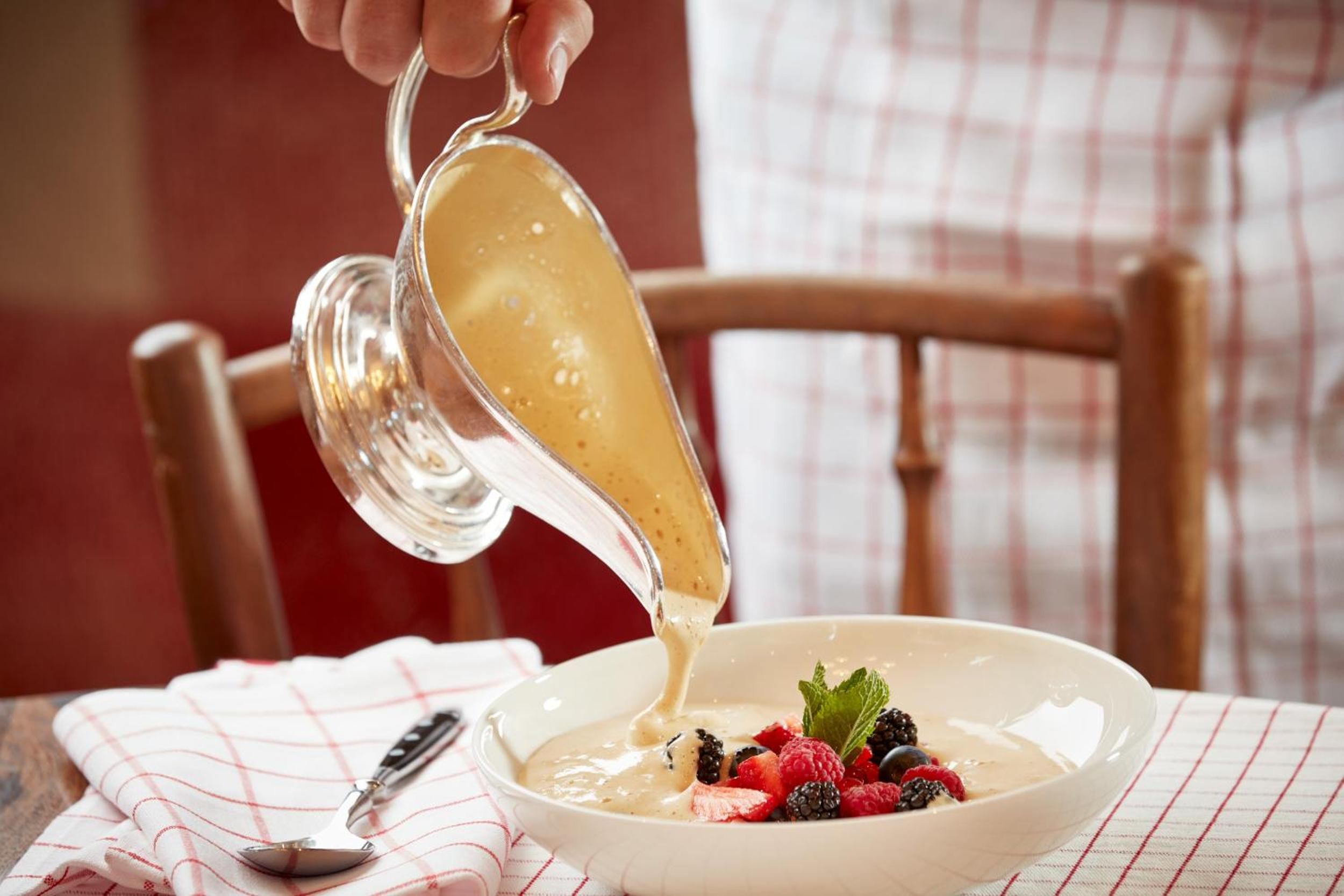 Golden custard cascades from crystal glass onto fresh berries, as sunlight streams through windows illuminating this artful dessert presentation in the hotel's refined dining room.