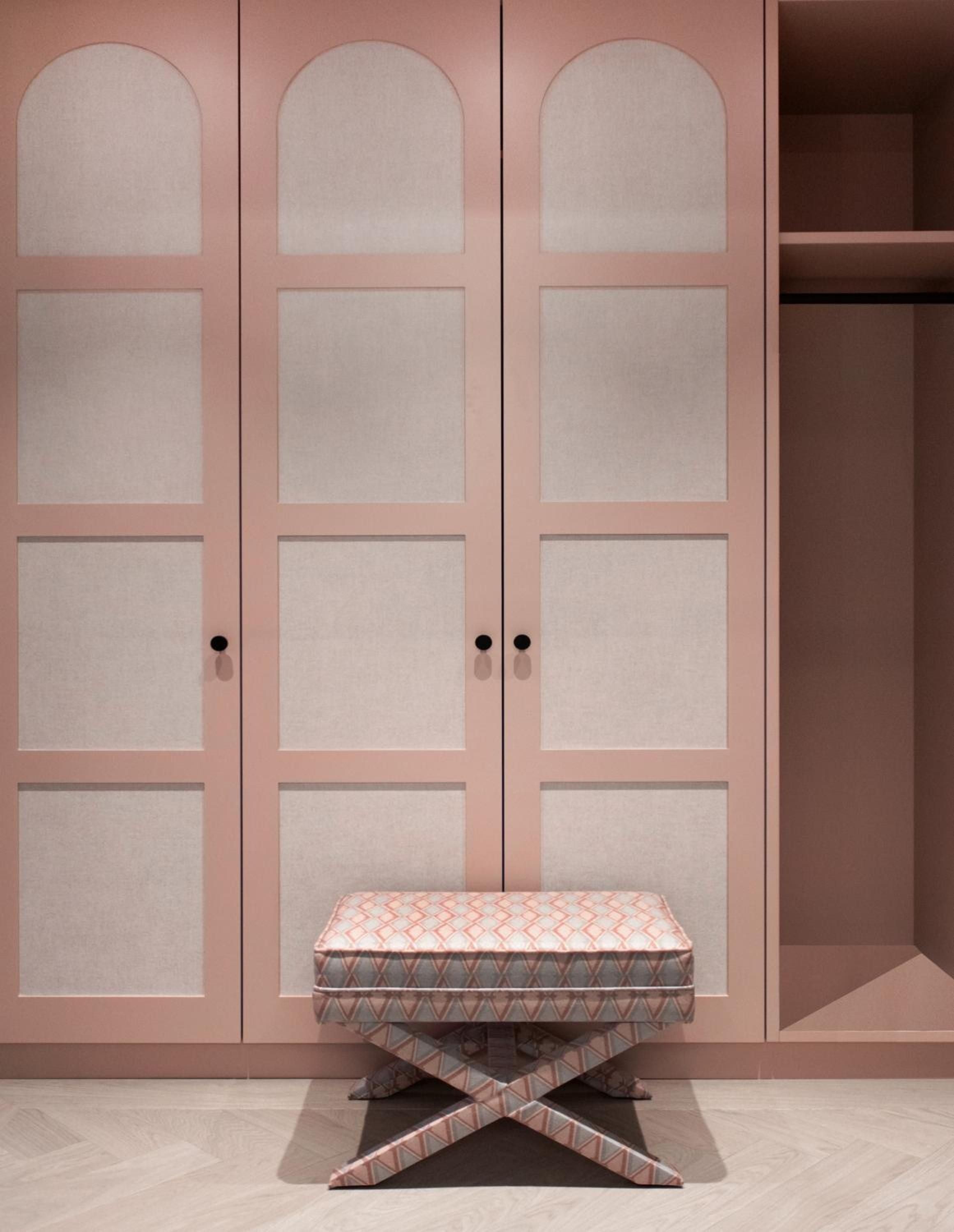 Blush-toned built-in wardrobes frame a geometric ottoman in this thoughtfully designed guest suite, where soft pink hues create an unexpectedly sophisticated sanctuary.