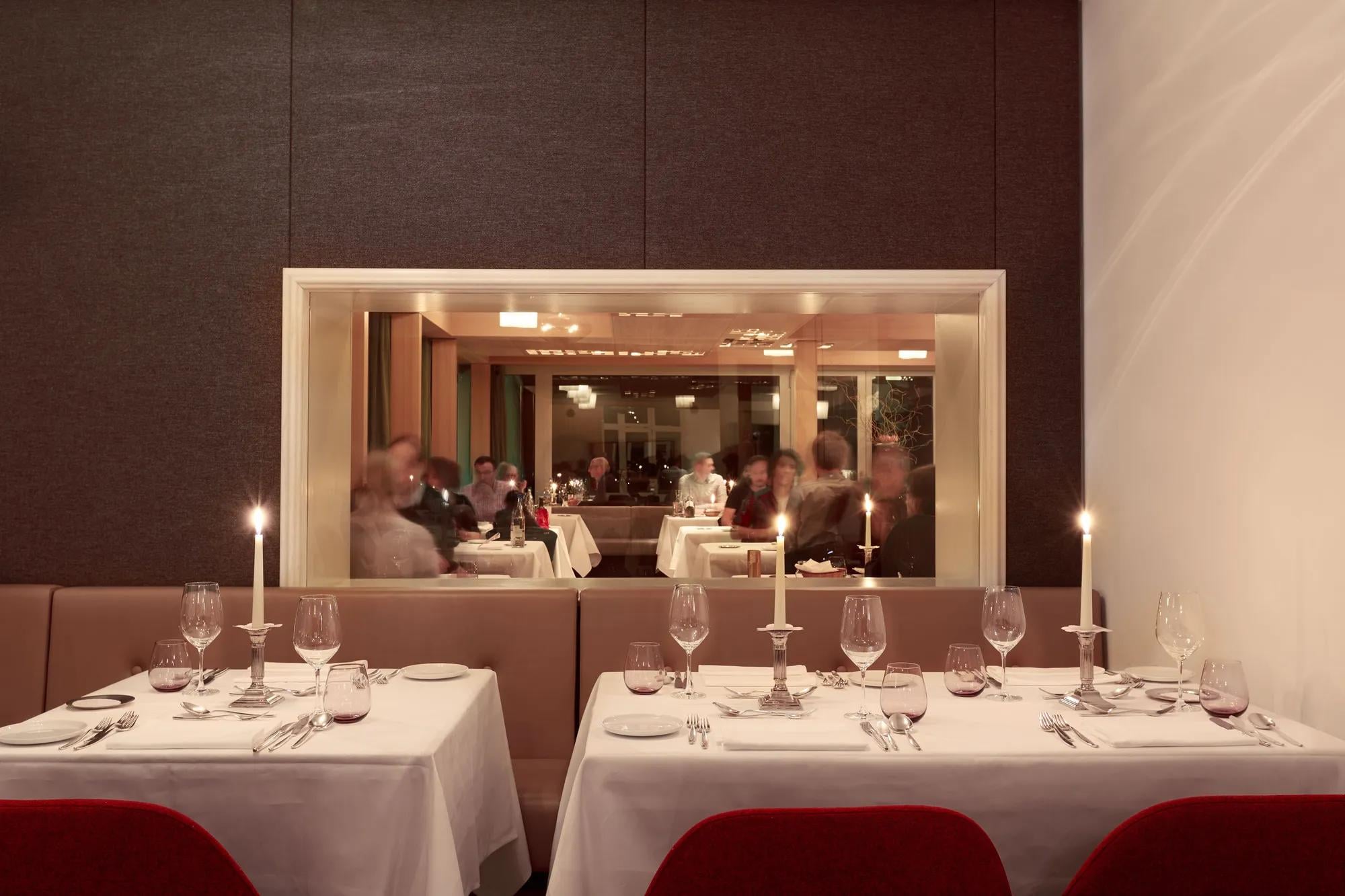 Candlelit tables and warm amber lighting create an intimate dining atmosphere, where the open kitchen view through sleek glass adds theatrical energy to every meal.