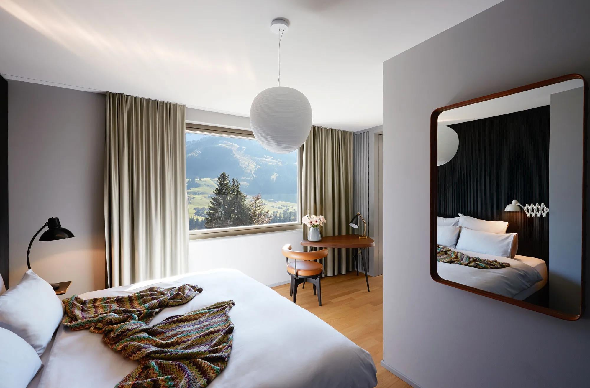 Mountain vistas frame this serene guest room where warm wood floors meet contemporary furnishings, creating an Alpine sanctuary with panoramic views of rolling green valleys.