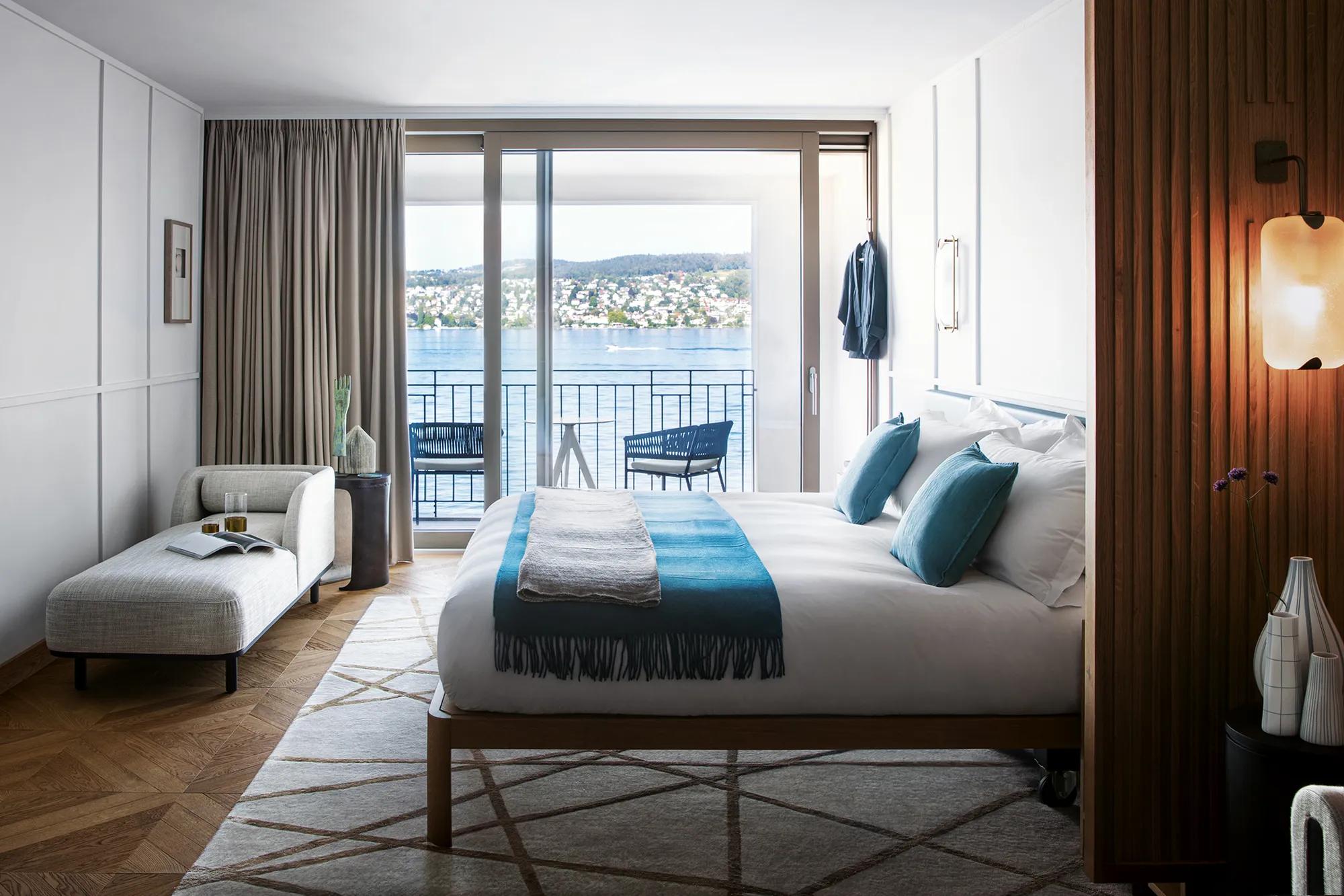 Lake Zurich stretches beyond floor-to-ceiling windows in this serene suite, where teal accents echo the water's hue and warm wood paneling creates intimate lakeside luxury.