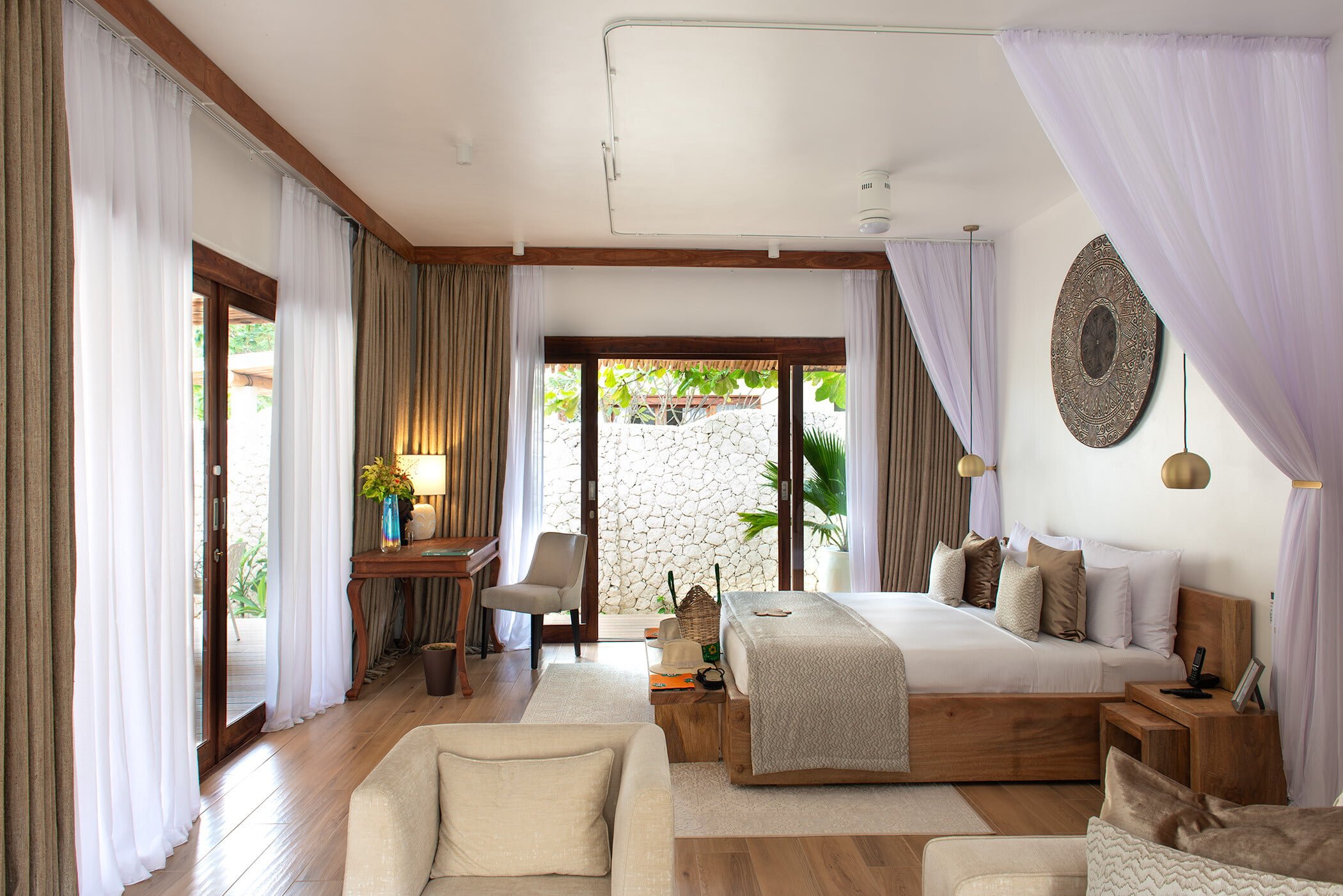 Billowing white canopies frame this serene suite where warm wood tones meet coral stone walls, creating an intimate sanctuary with direct garden access.