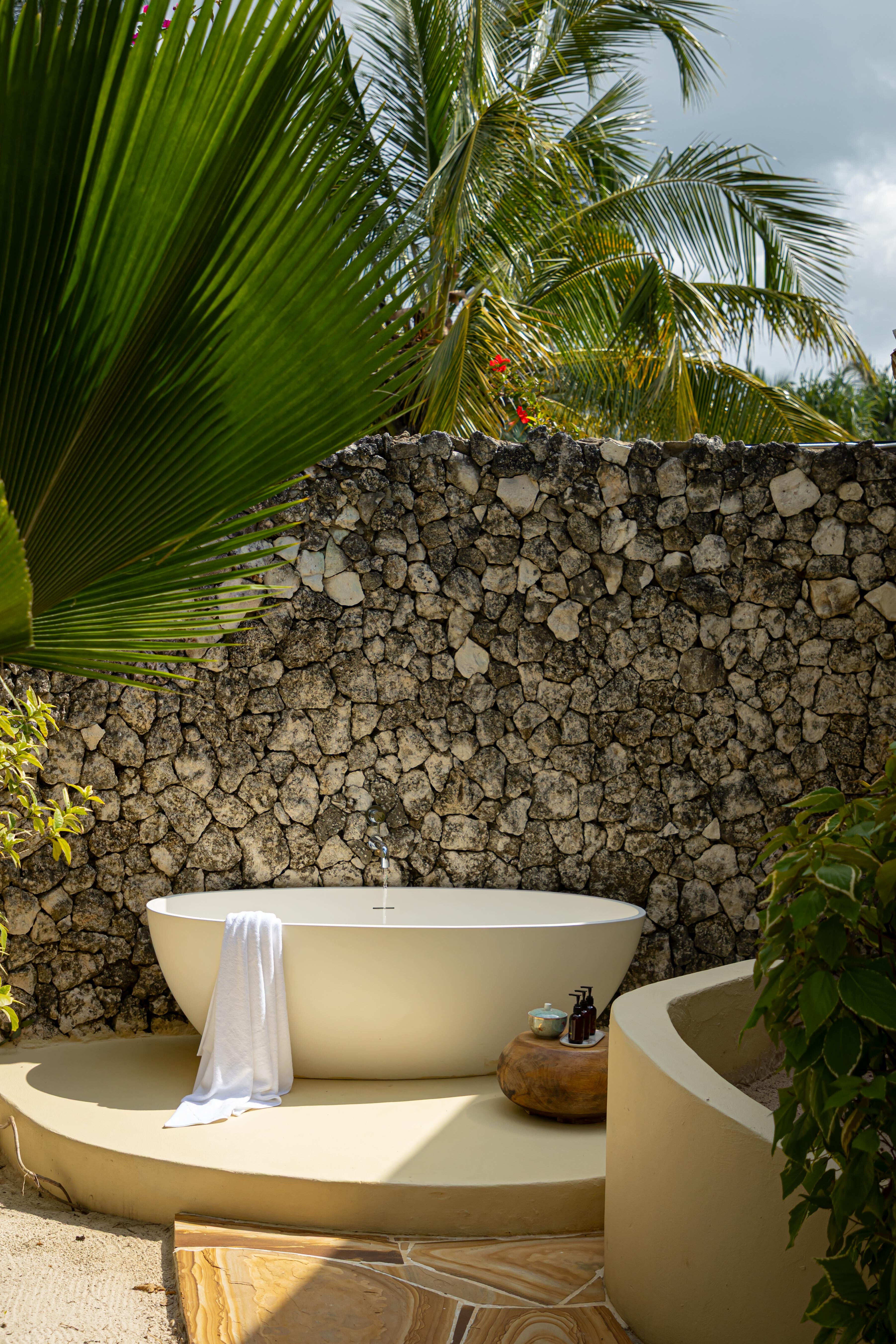 Volcanic stone walls frame a sculptural soaking tub where tropical breezes carry palm whispers, creating an intimate open-air sanctuary for evening rituals.