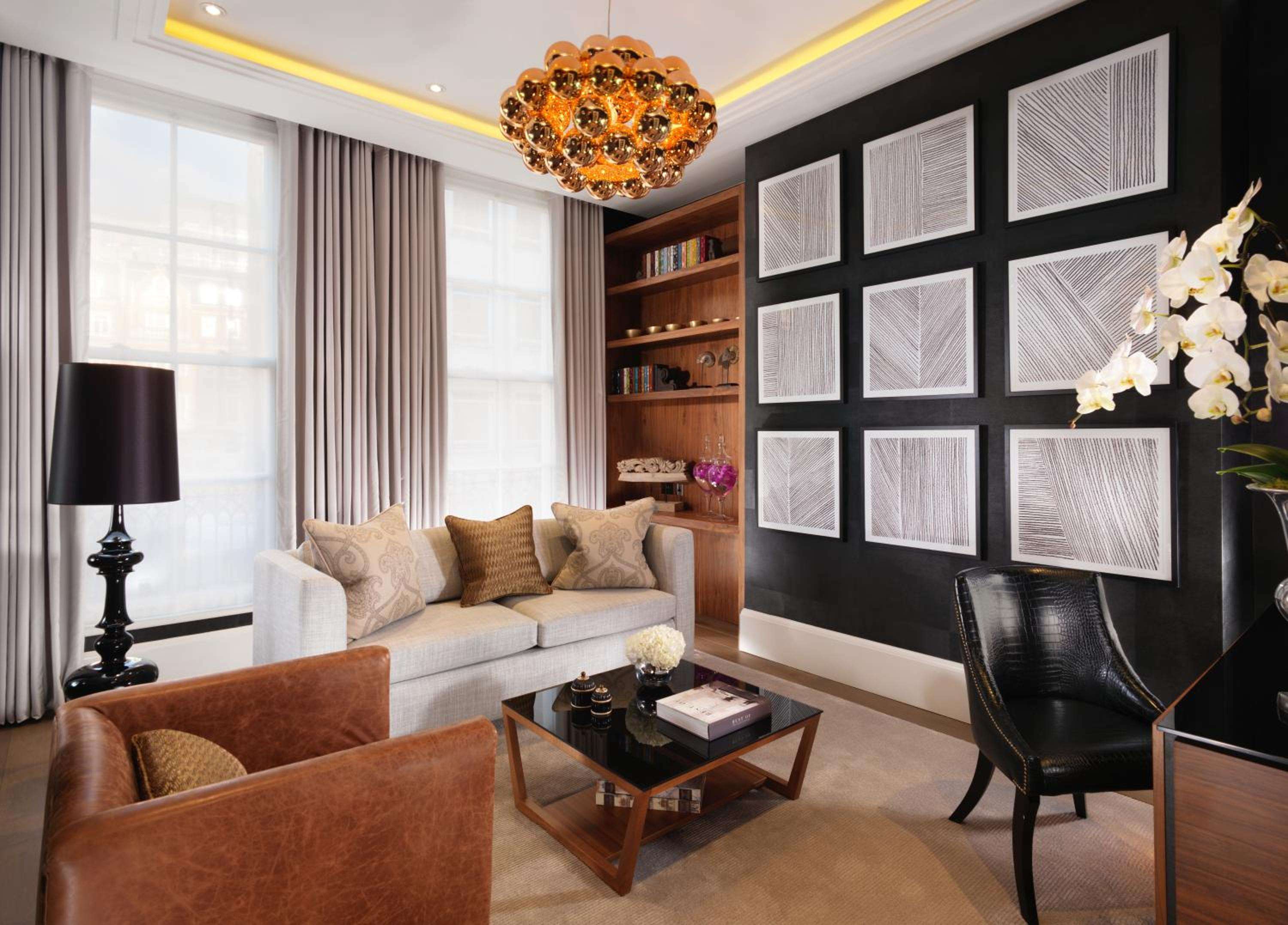 Rich cognac leather and geometric artwork create intimate elegance in this sophisticated sitting area, where amber chandeliers cast warm pools of light across polished surfaces.
