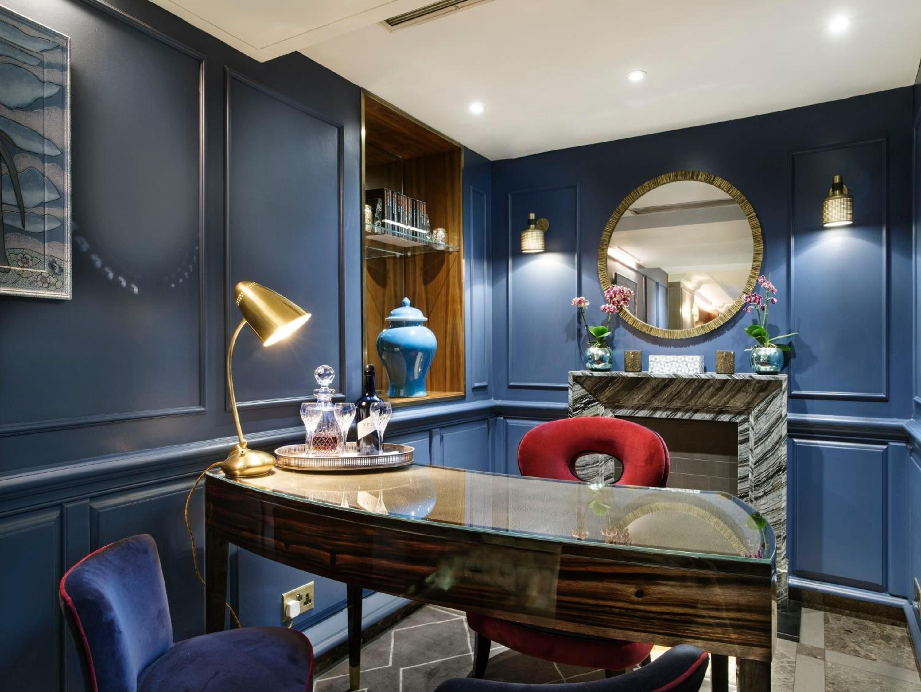 Navy paneled walls create an intimate cocoon around the polished desk where golden task lighting mingles with crystal decanters and rich velvet seating.