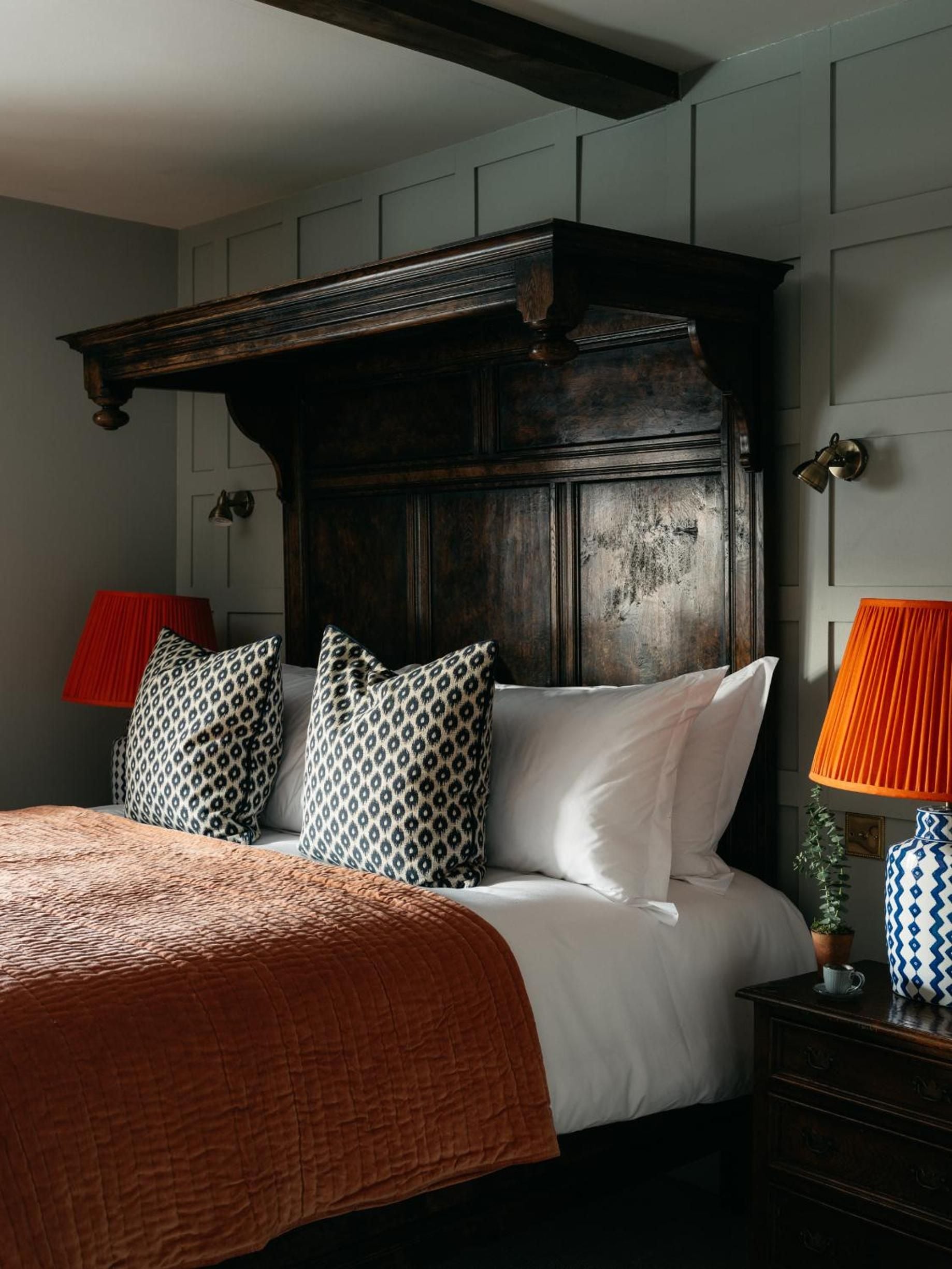 Dark timber paneling and geometric cushions create intimate charm, while orange lampshades cast a warm glow against sage-green walls in this thoughtfully curated retreat.