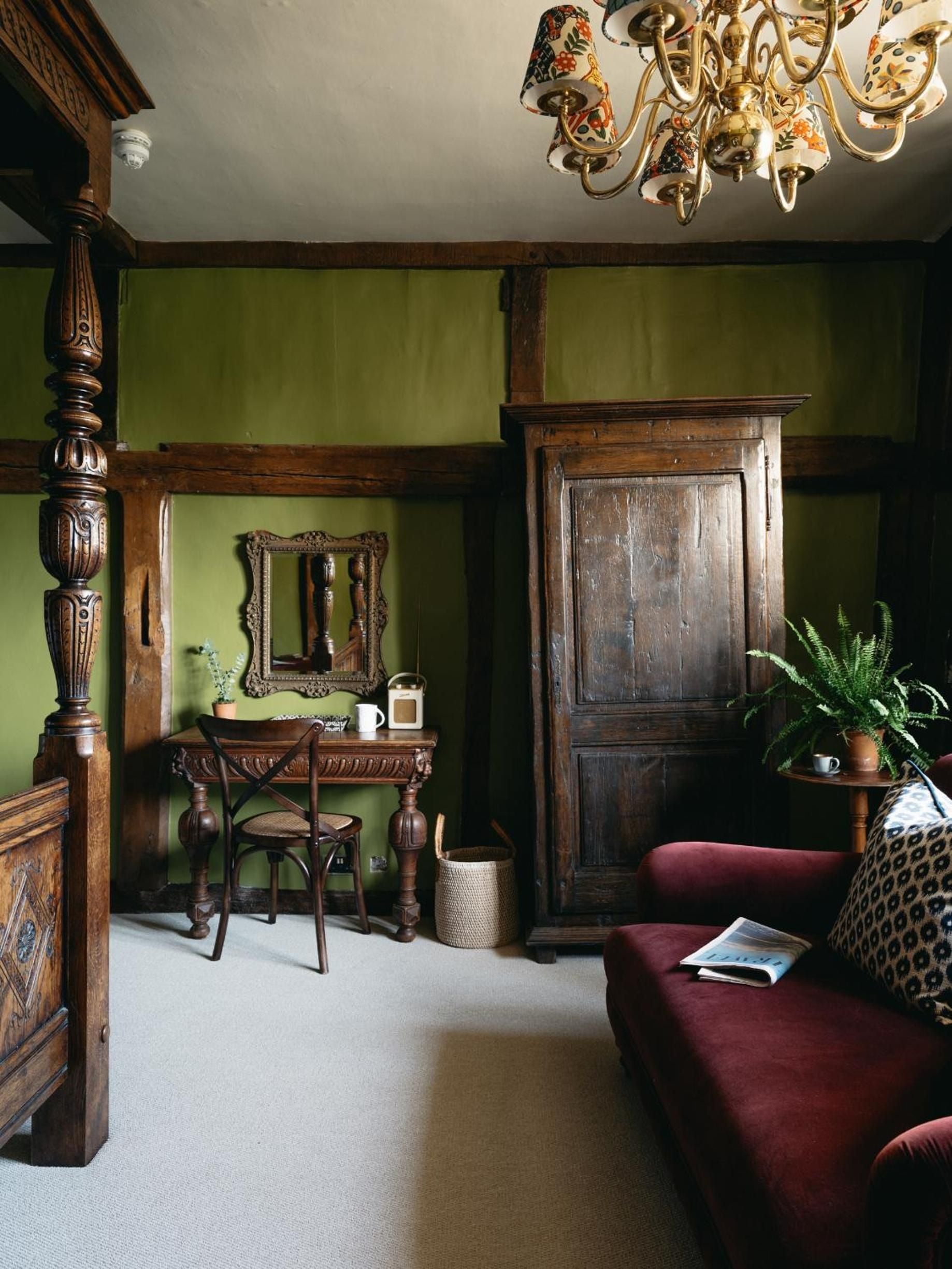 Carved oak beams and sage-green walls create an intimate study corner, where antique furnishings and a whimsical chandelier blend Tudor heritage with contemporary comfort.