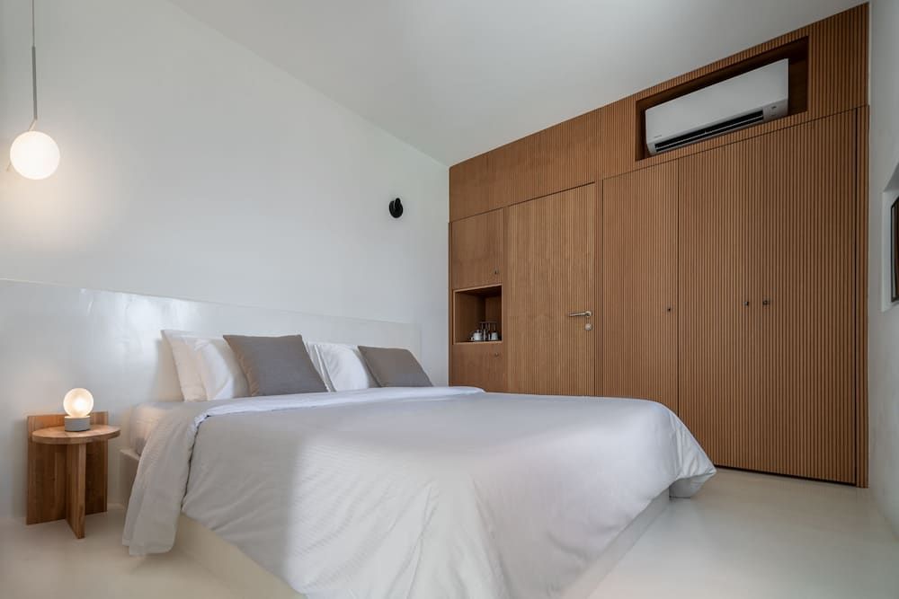 Warm wood paneling embraces crisp white linens in this serene suite, where minimalist design meets Mediterranean warmth through clever built-in storage and ambient lighting.