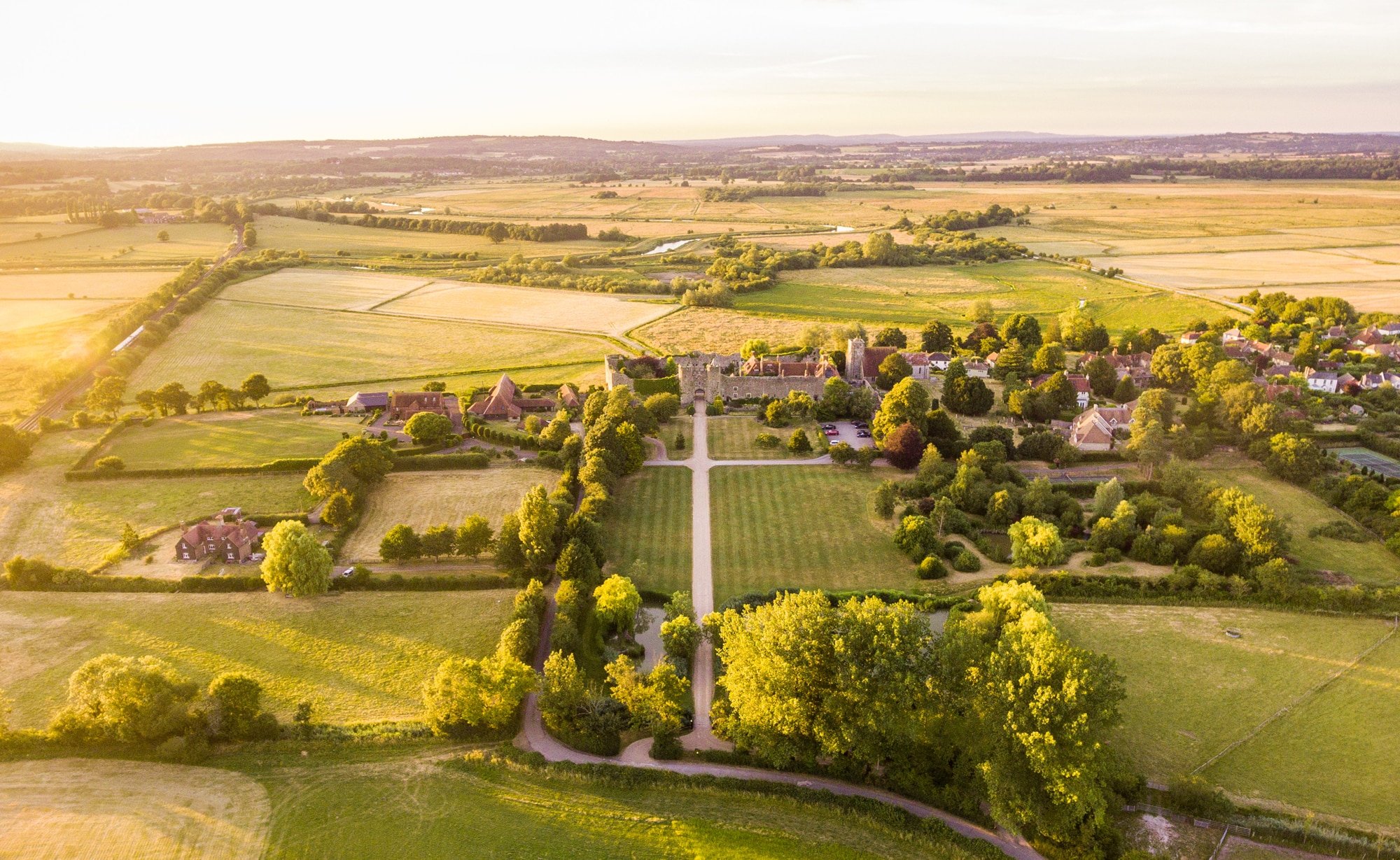 Golden hour illuminates the medieval fortress and its manicured grounds, where centuries-old stone walls rise from emerald lawns stretching toward the Sussex countryside.