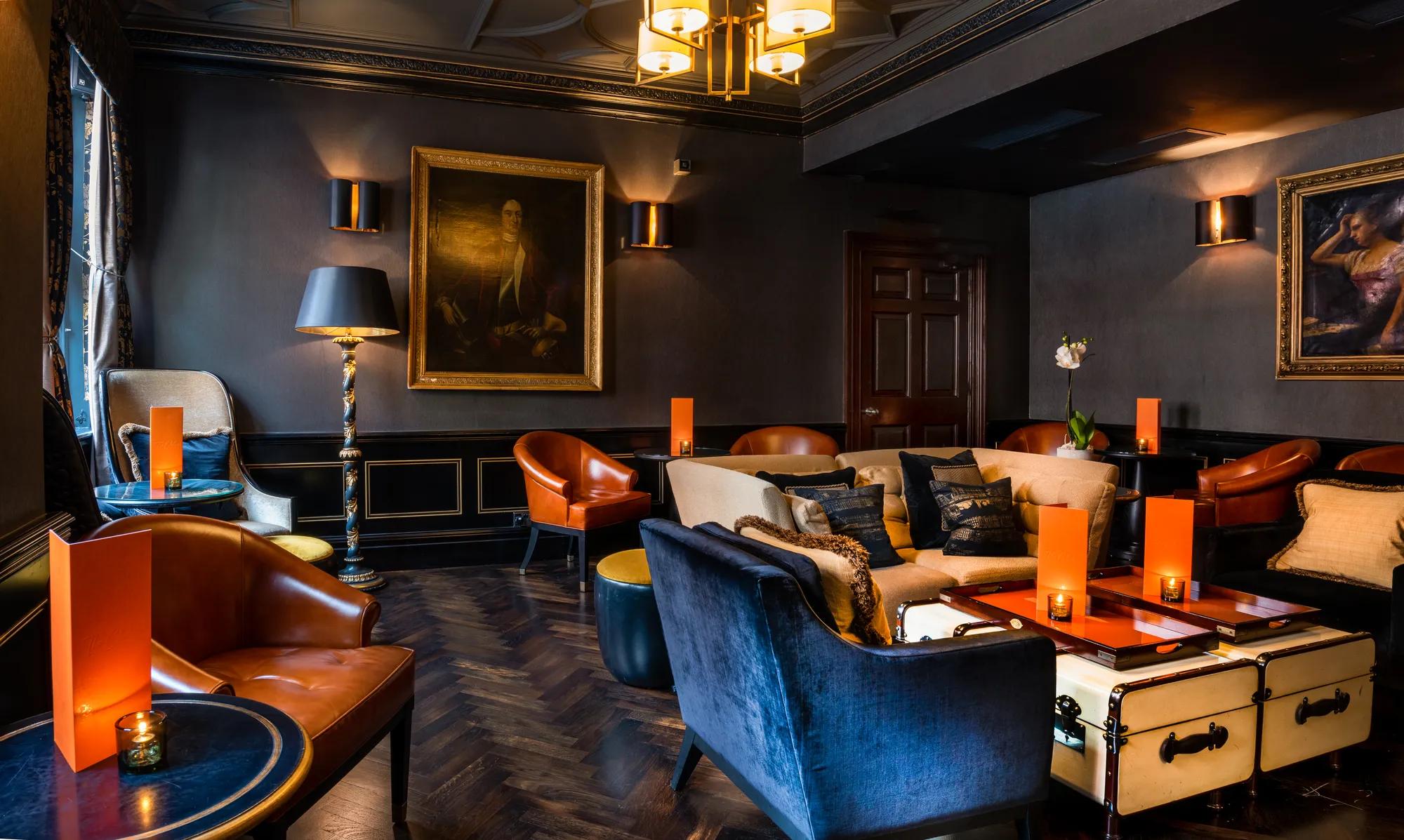 Warm amber light illuminates cognac leather chairs and navy velvet sofas in this moody lounge, where classical portraits oversee intimate conversations over vintage trunks.