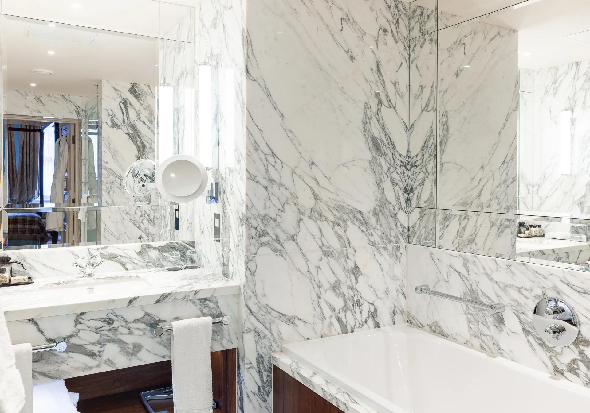 Book-matched Calacatta marble creates dramatic veining patterns across walls and surfaces, while polished chrome fixtures catch natural light streaming through tall windows.