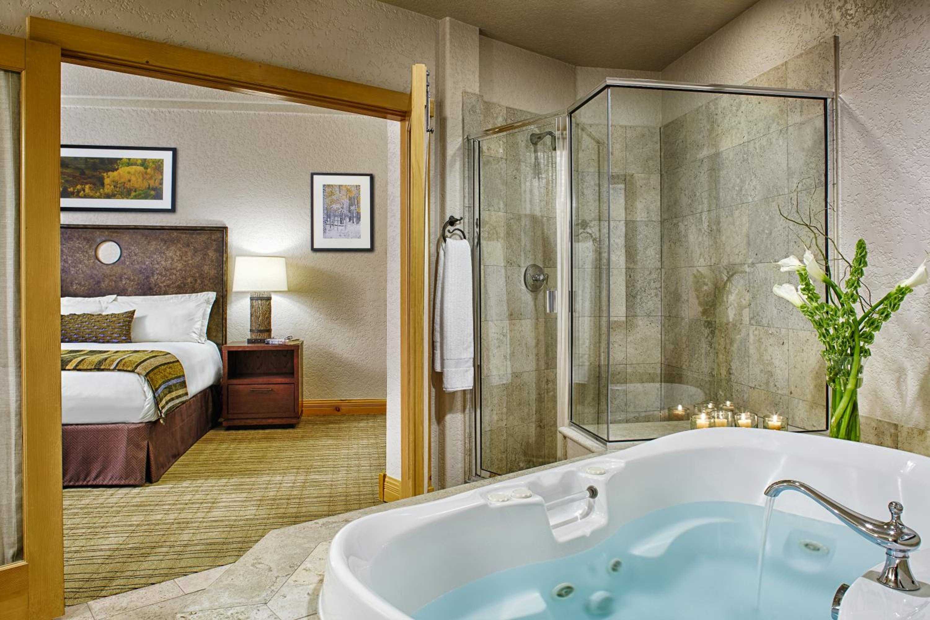 Warm wood frames separate the sleeping quarters from an indulgent soaking tub, while stone-lined shower walls create an intimate spa sanctuary within your suite.