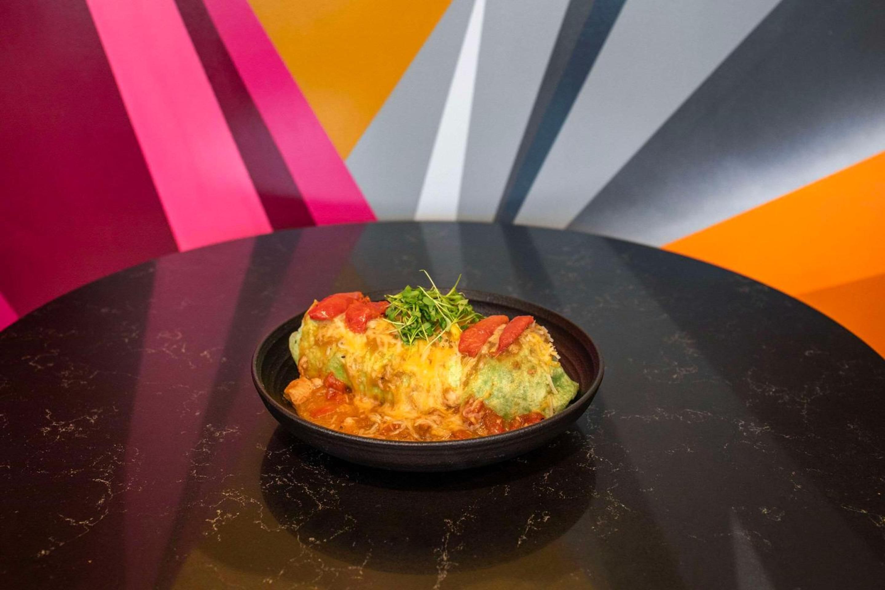 Vibrant cast-iron sizzling fajitas arrive tableside against a backdrop of bold geometric murals, showcasing the hotel's contemporary culinary flair and artistic design sensibility.
