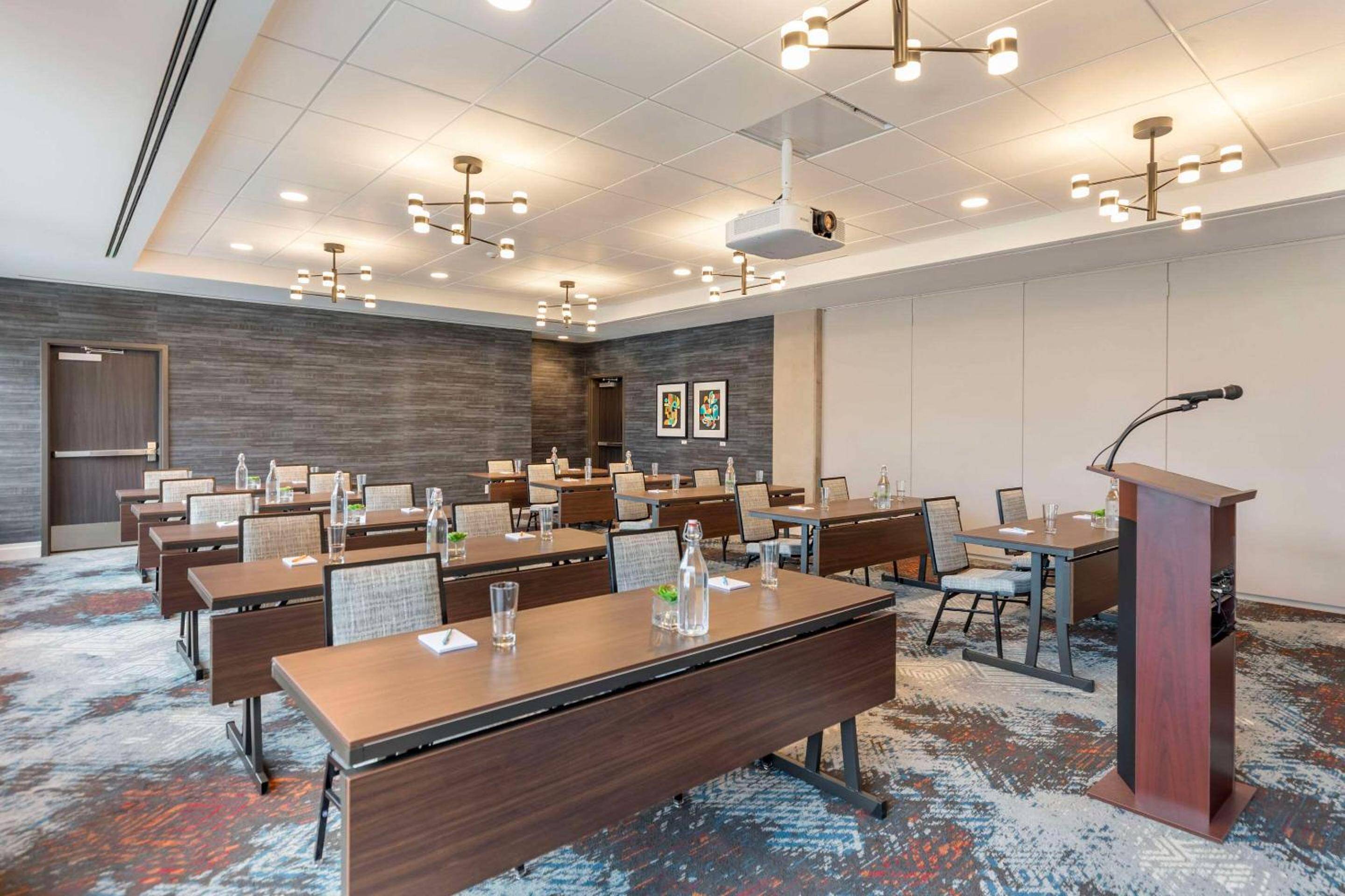 Modern chandeliers cast warm light over classroom-style seating in this sophisticated conference space, where textured stone walls meet contemporary furnishings for productive gatherings.