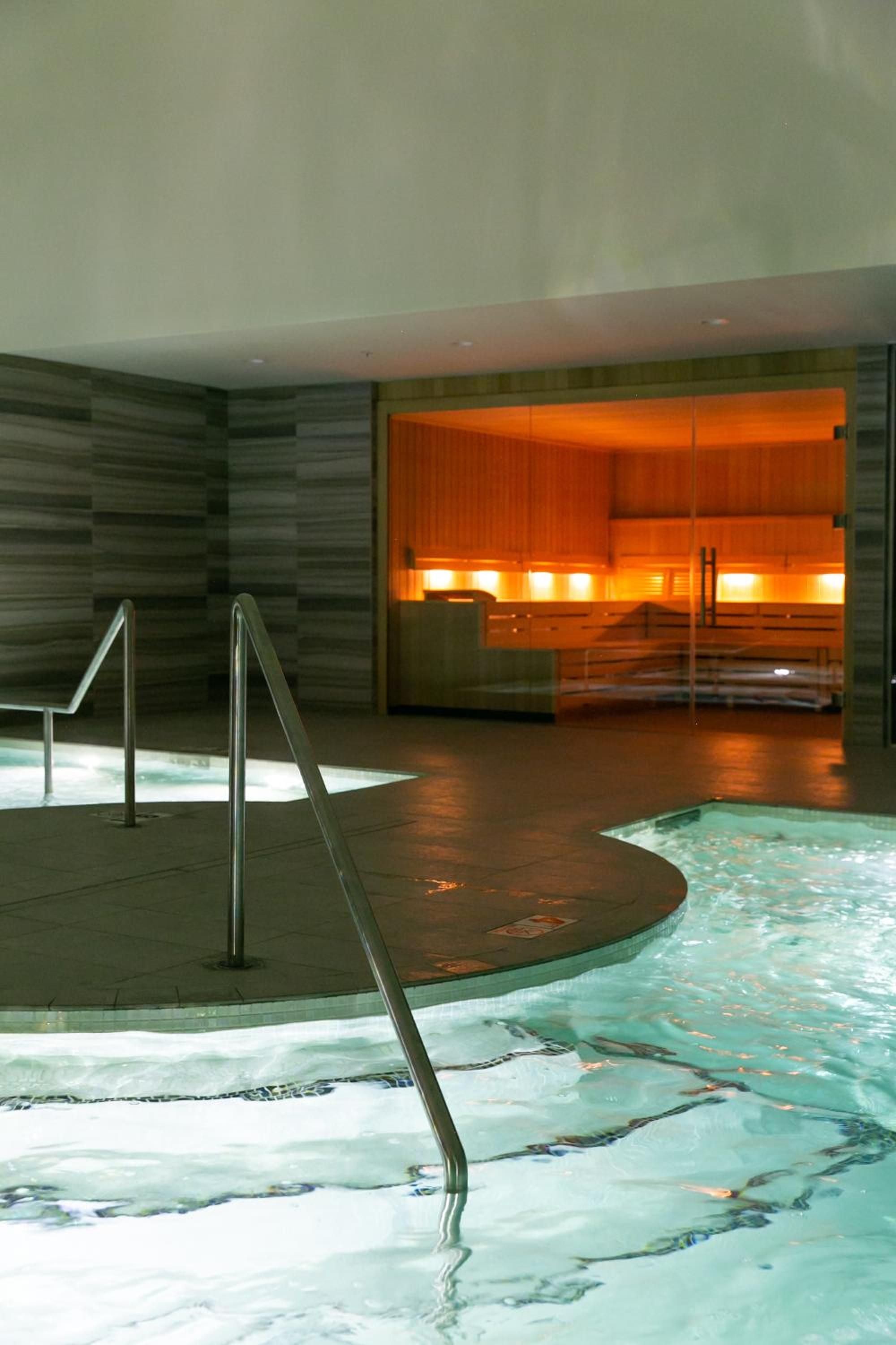 Amber-lit sauna warmth beckons beyond the sunken hydrotherapy pools, where sleek handrails guide guests through this temple of modern wellness and ancient ritual.