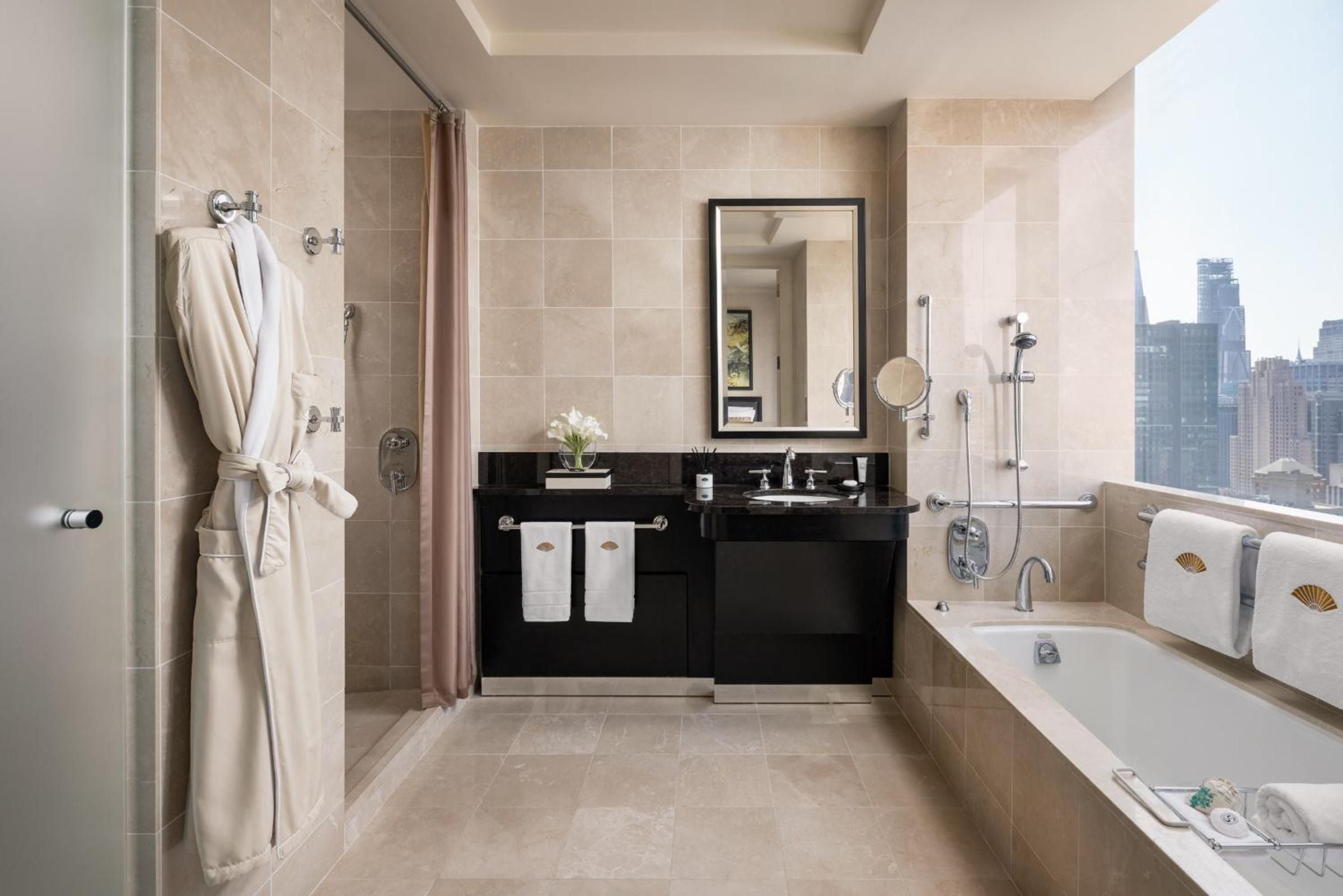 Limestone surfaces and black granite create spa-like serenity in this corner suite bathroom, where soaking tubs frame stunning Manhattan skyline views.