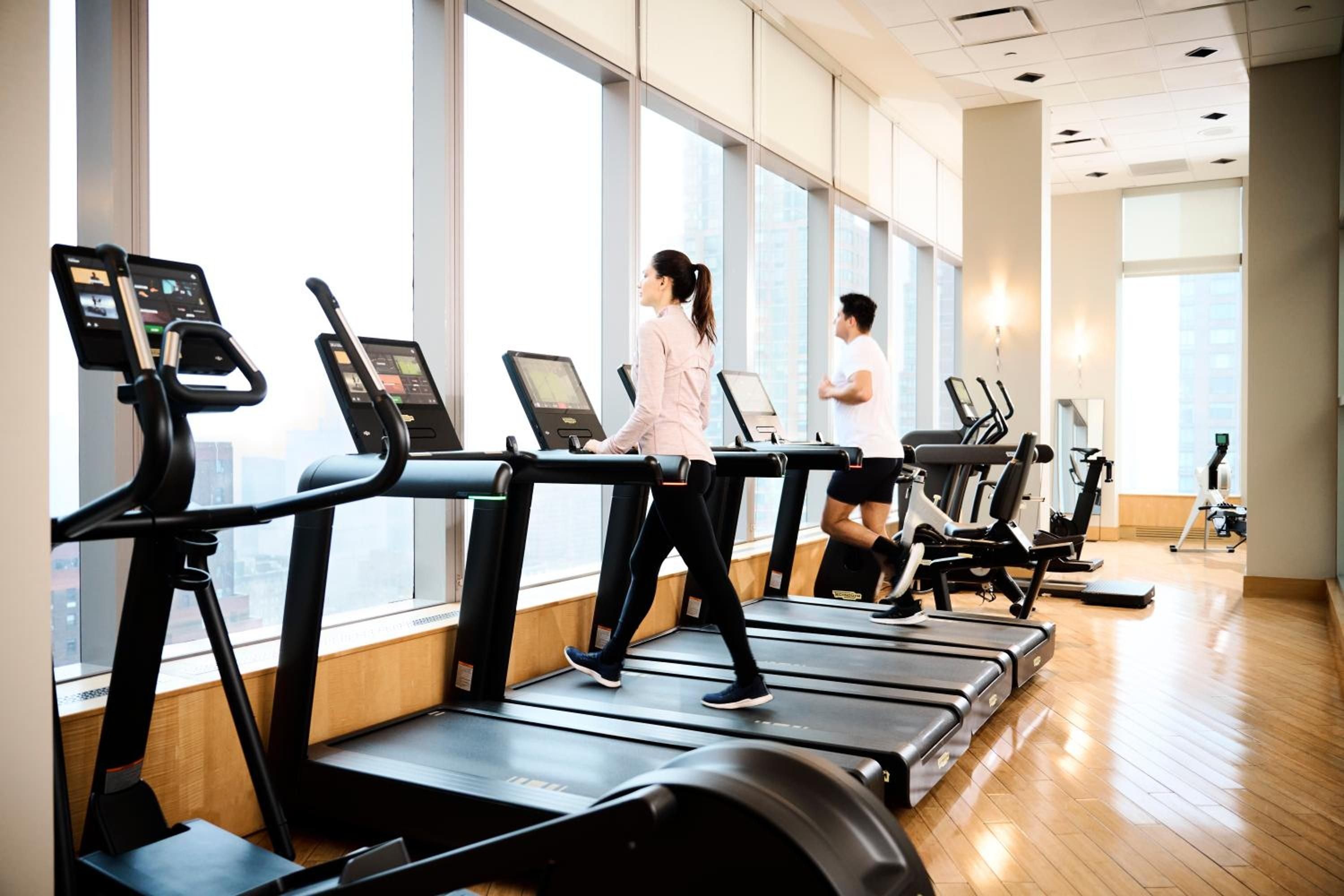 Floor-to-ceiling windows frame Manhattan's skyline as guests stride through their morning routine on state-of-the-art treadmills, polished hardwood gleaming beneath their feet.