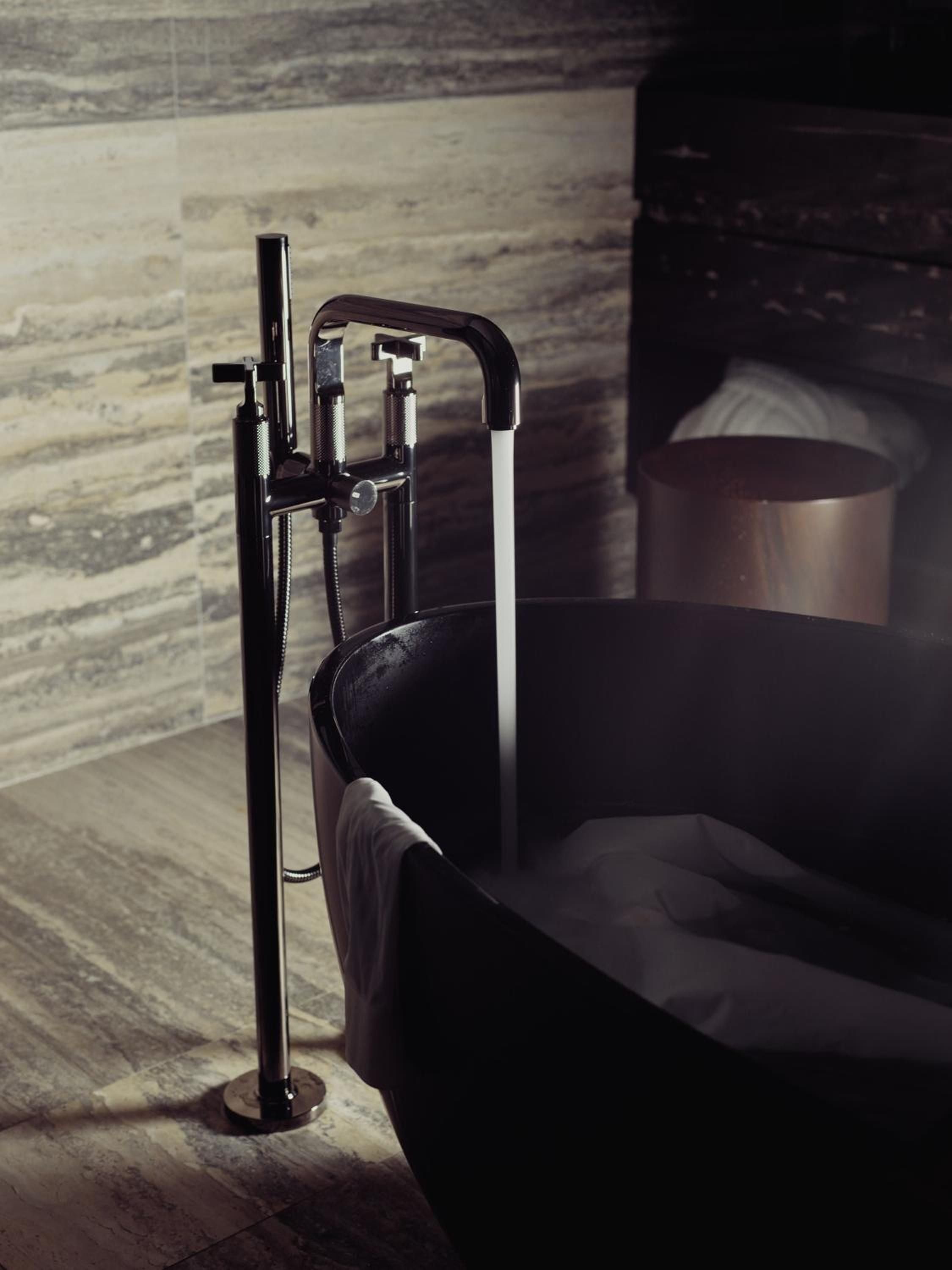 Sleek floor-mounted tub filler commands attention beside a sculptural black stone soaking tub, where polished chrome meets raw marble in sophisticated contrast.