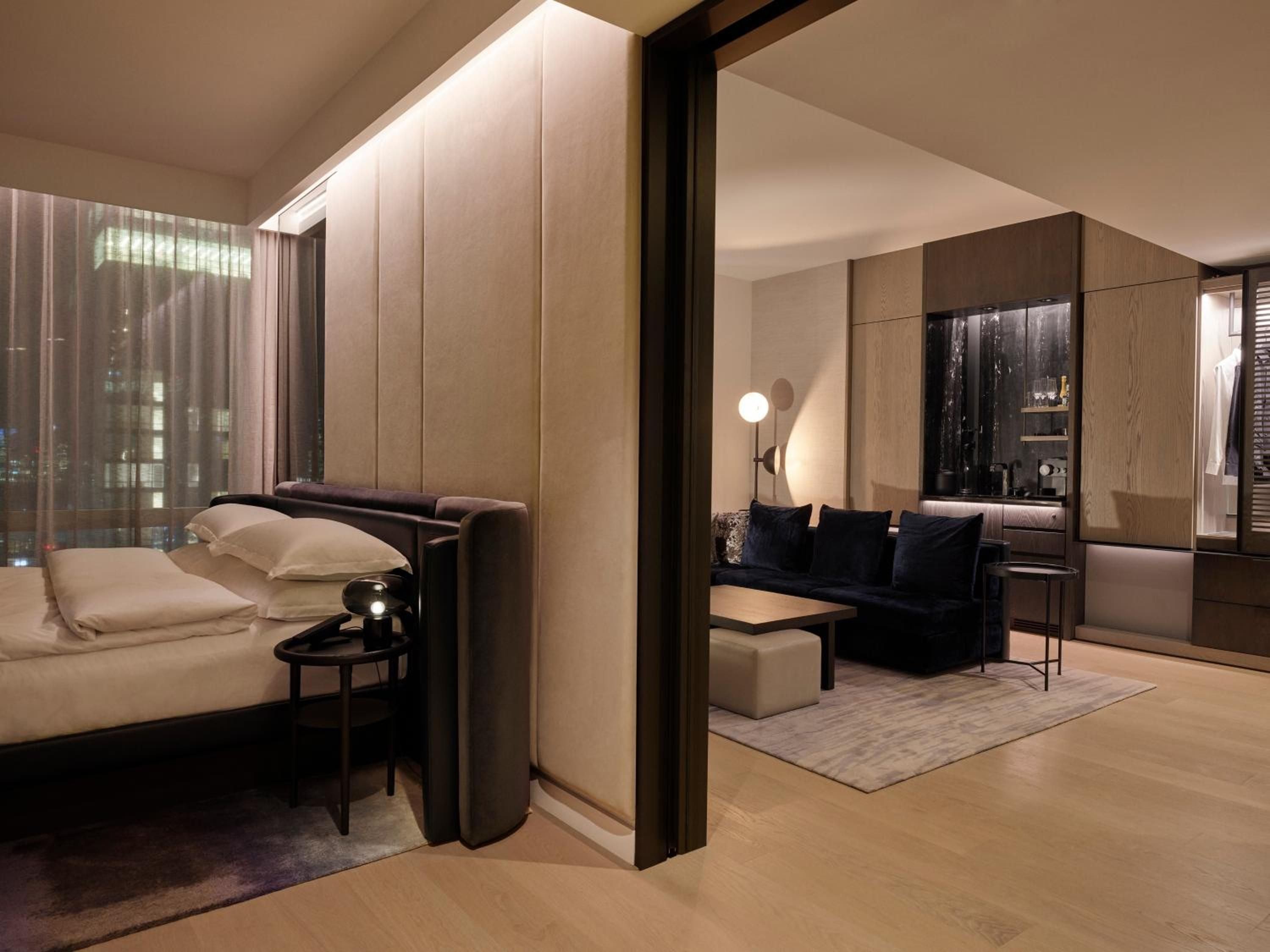 Warm wood tones and sophisticated navy accents create an intimate sanctuary where the bedroom flows seamlessly into a chic living area through sleek sliding panels.