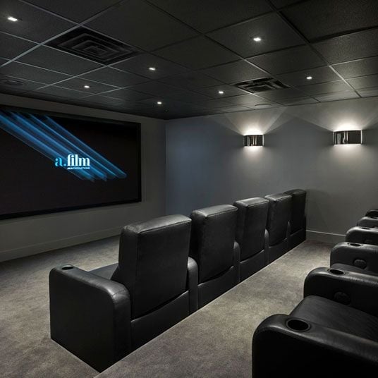 Plush leather recliners face a wall-mounted screen in this intimate screening room, where recessed lighting and charcoal walls create perfect cinematic ambiance.