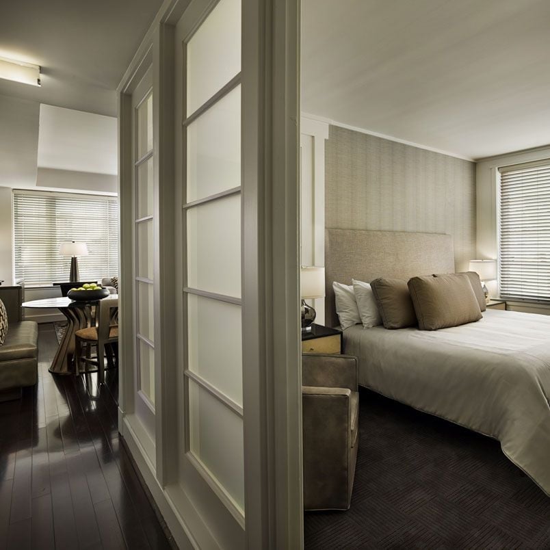 Sliding frosted glass doors separate the plush bedroom from the dining area, creating intimate spaces within the sophisticated neutral-toned suite.