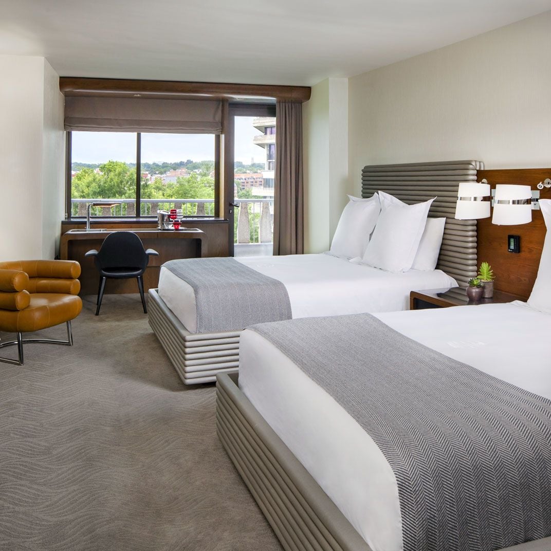 Ridged headboards and warm wood accents frame twin beds in this Georgetown retreat, where floor-to-ceiling windows reveal leafy cityscapes beyond the private balcony.